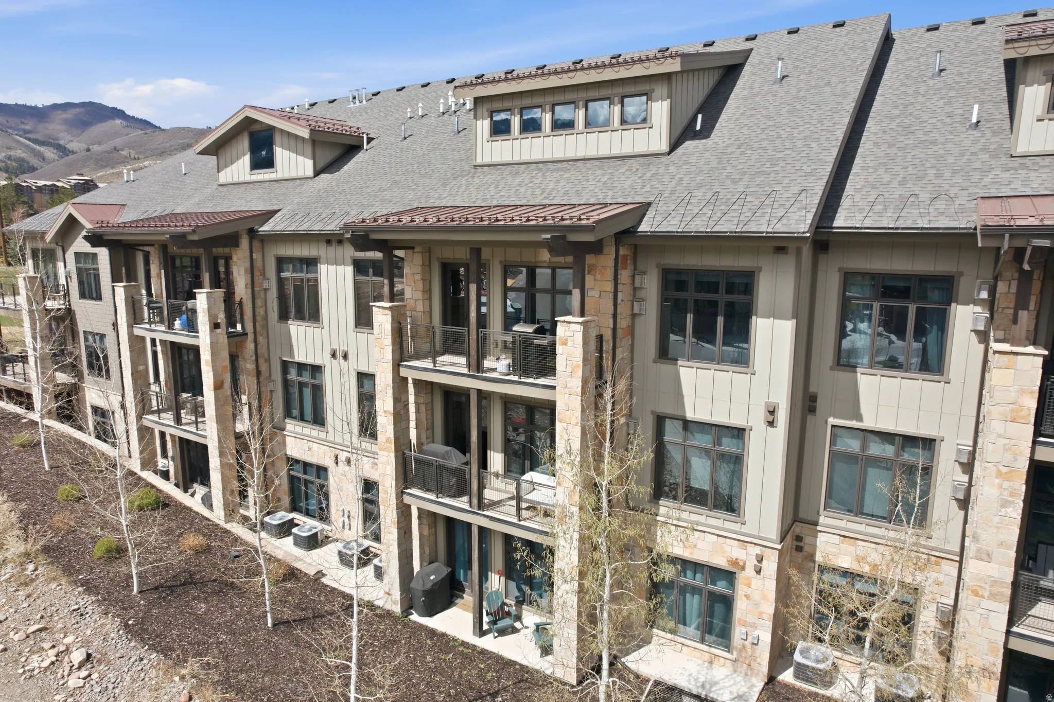 Multi-story building featuring stone and siding exterior, multiple balconies, dark-framed windows, and sloped roofing with dormers