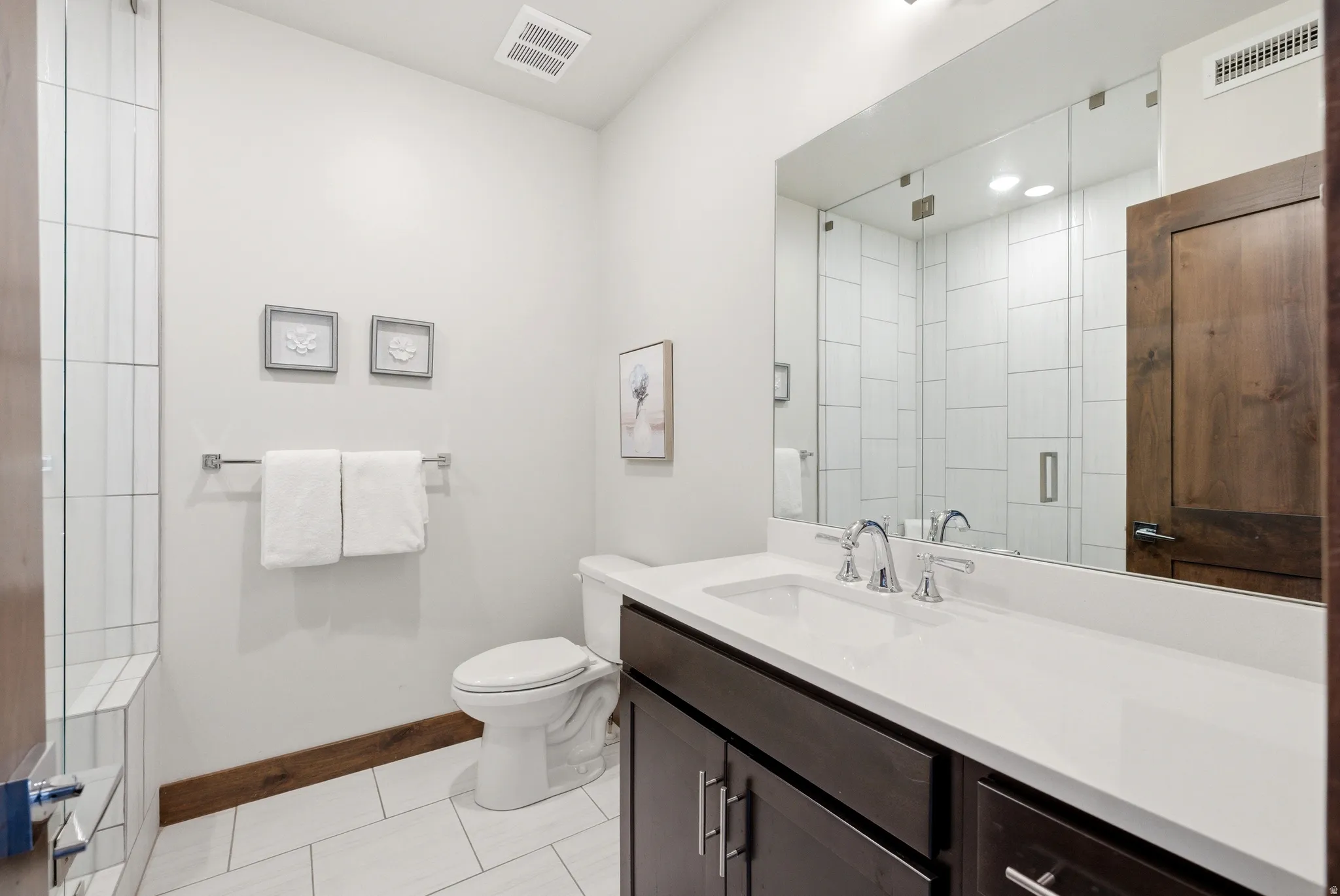 Contemporary bathroom featuring a dark wood-finish vanity with an integrated white sink, chrome fixtures, and a frameless mirror