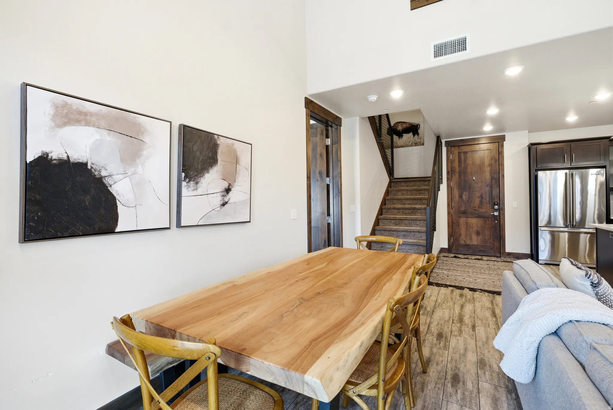 Open-concept living area featuring high ceilings, recessed lighting, wood-finish flooring, a contemporary dining table, and a built-in stainless steel refrigerator