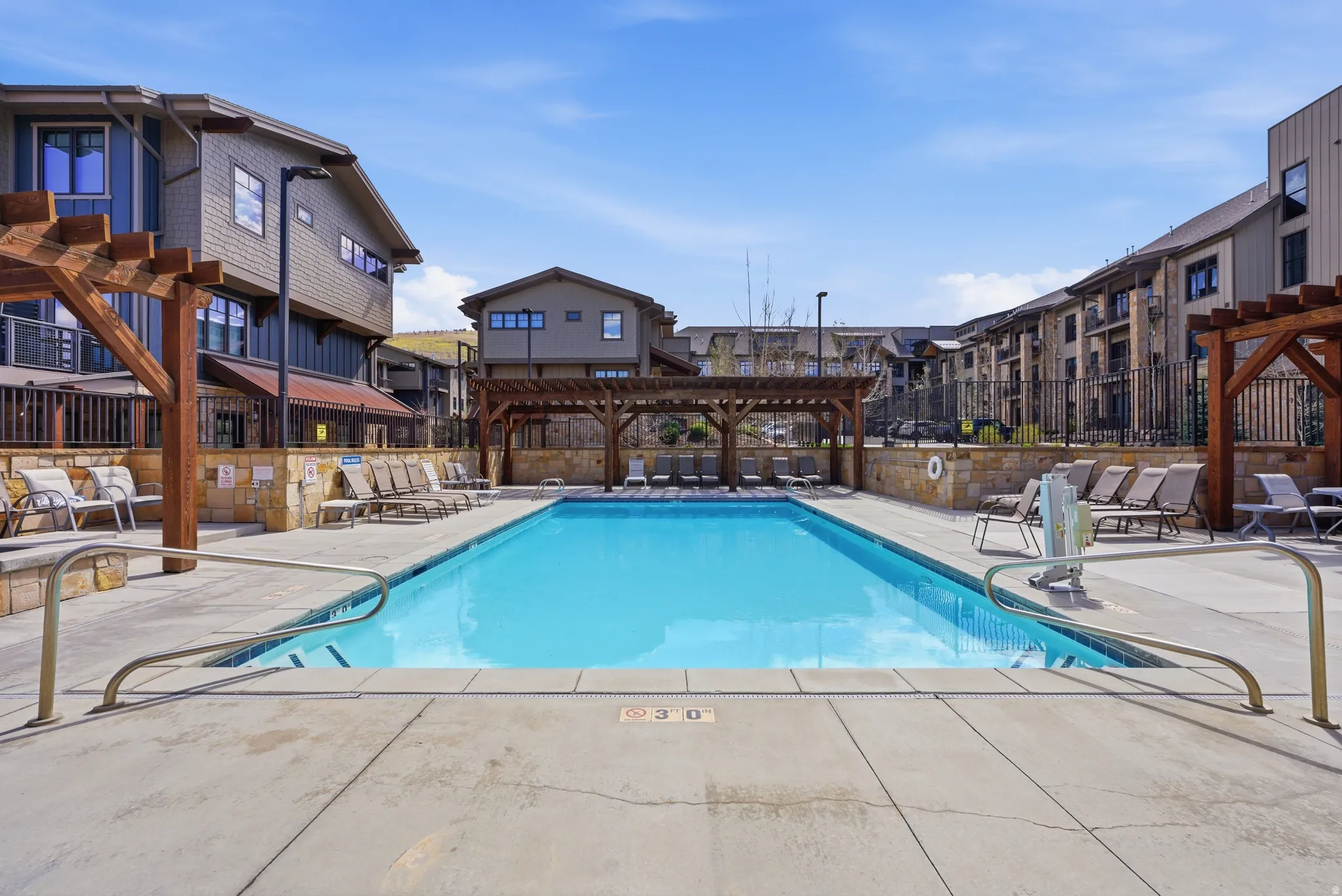 Outdoor swimming pool with concrete decking, surrounded by multiple pergolas, sun loungers, and stone-clad retaining walls