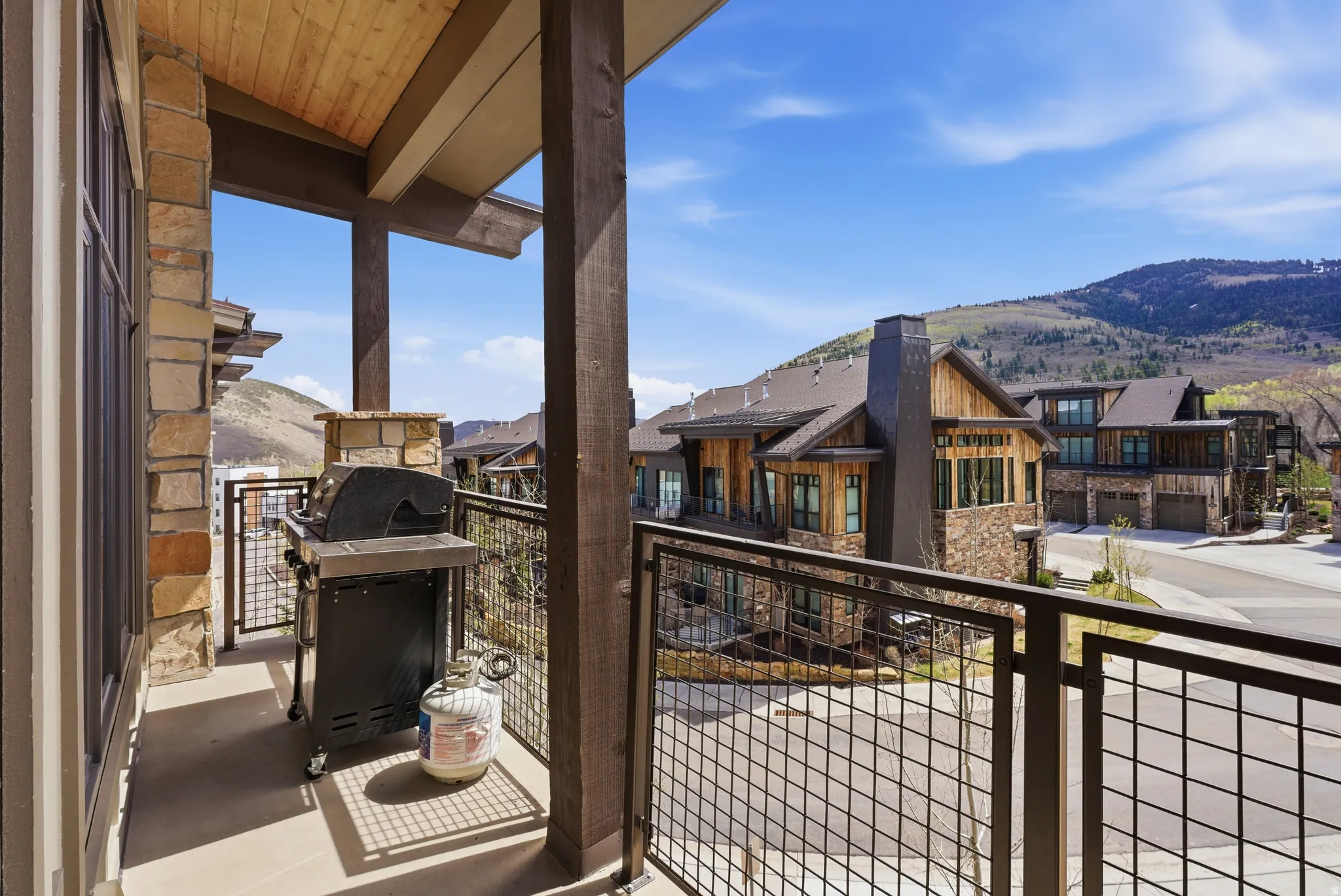 Private balcony featuring stone pillars, a wood-finish ceiling, and a metal grid railing