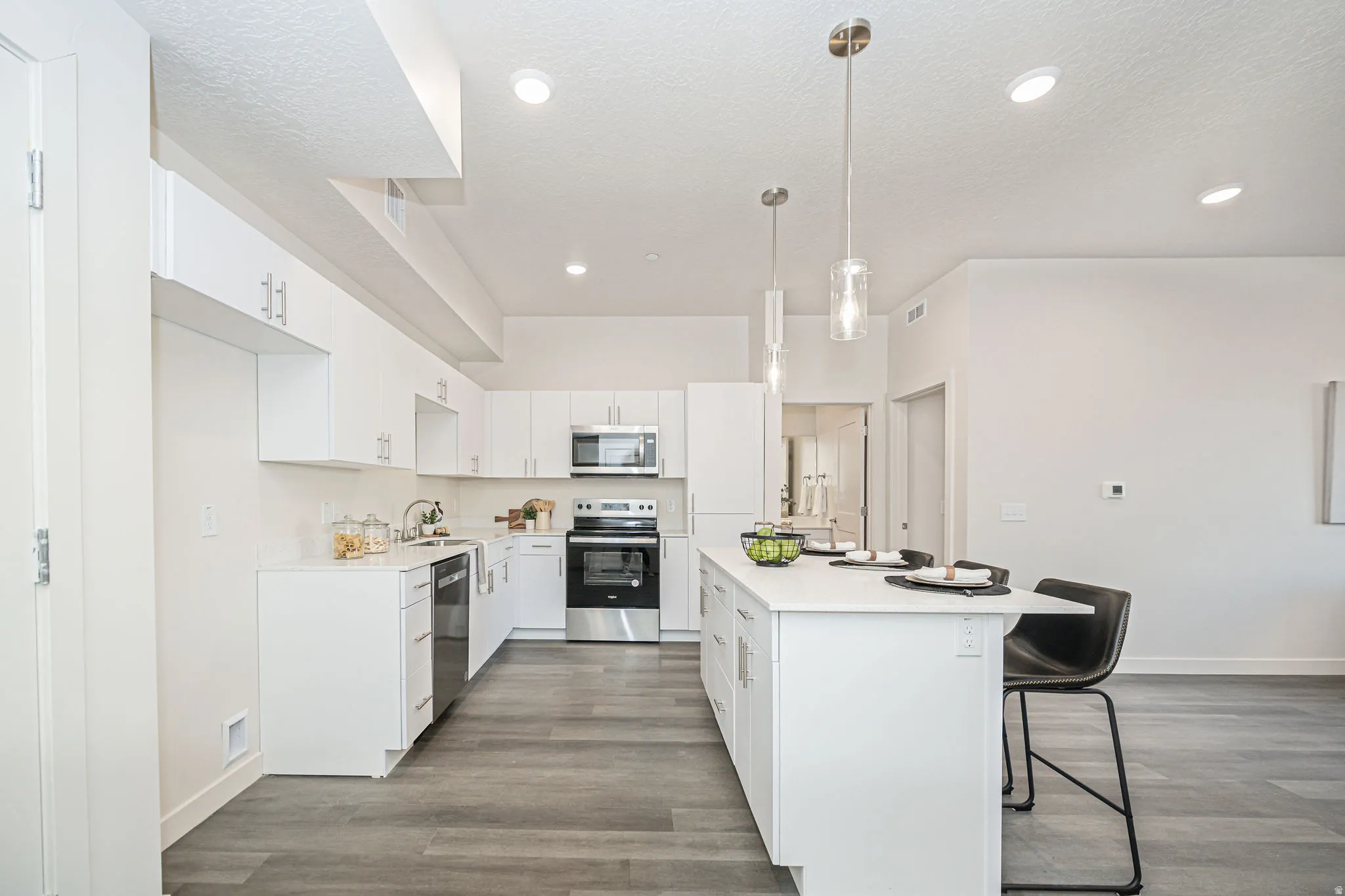 Kitchen with a breakfast bar area, white cabinetry, appliances with stainless steel finishes, hanging light fixtures, and dark wood-style flooring