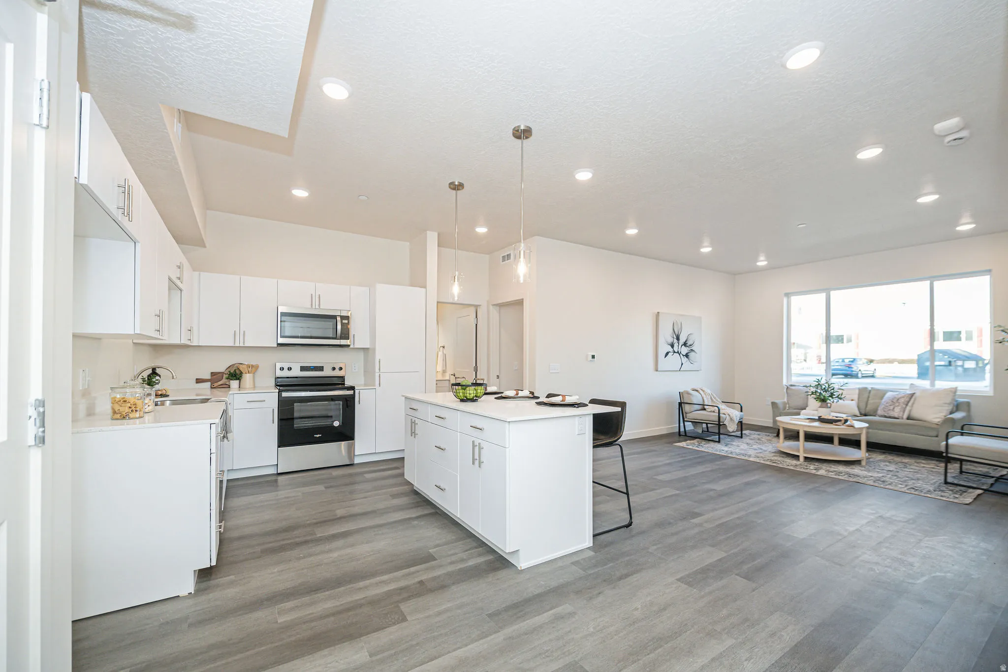 Kitchen with appliances with stainless steel finishes, open floor plan, a kitchen bar, white cabinets, and decorative light fixtures