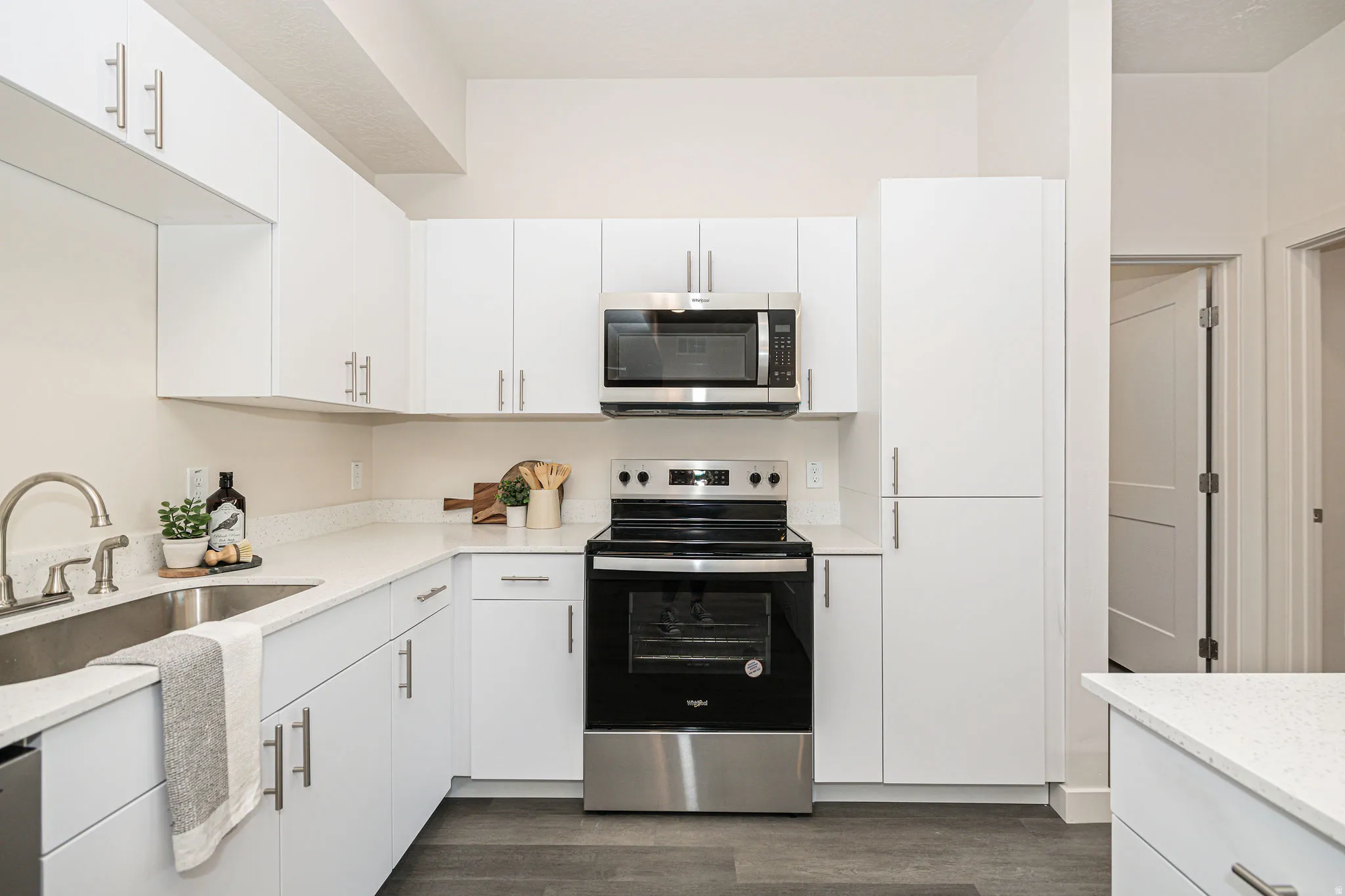 Kitchen featuring appliances with stainless steel finishes, white cabinetry, dark wood-style flooring, and light stone countertops