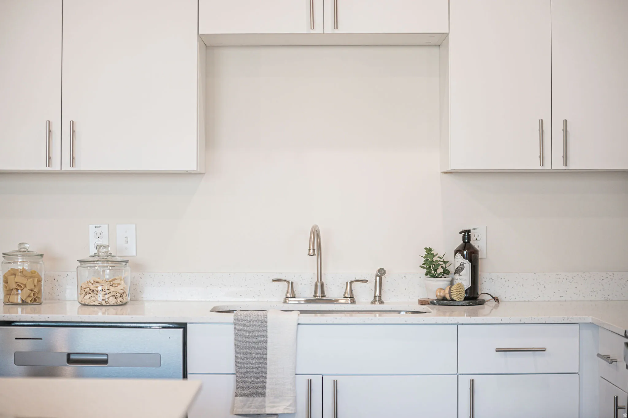 Kitchen featuring light stone countertops, white cabinetry, and stainless steel dishwasher
