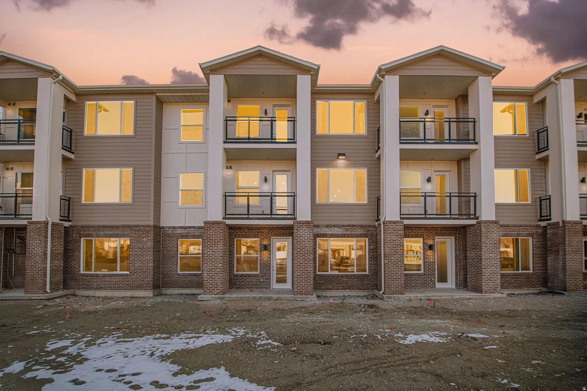 Back of property at dusk with brick siding, a patio, and a balcony