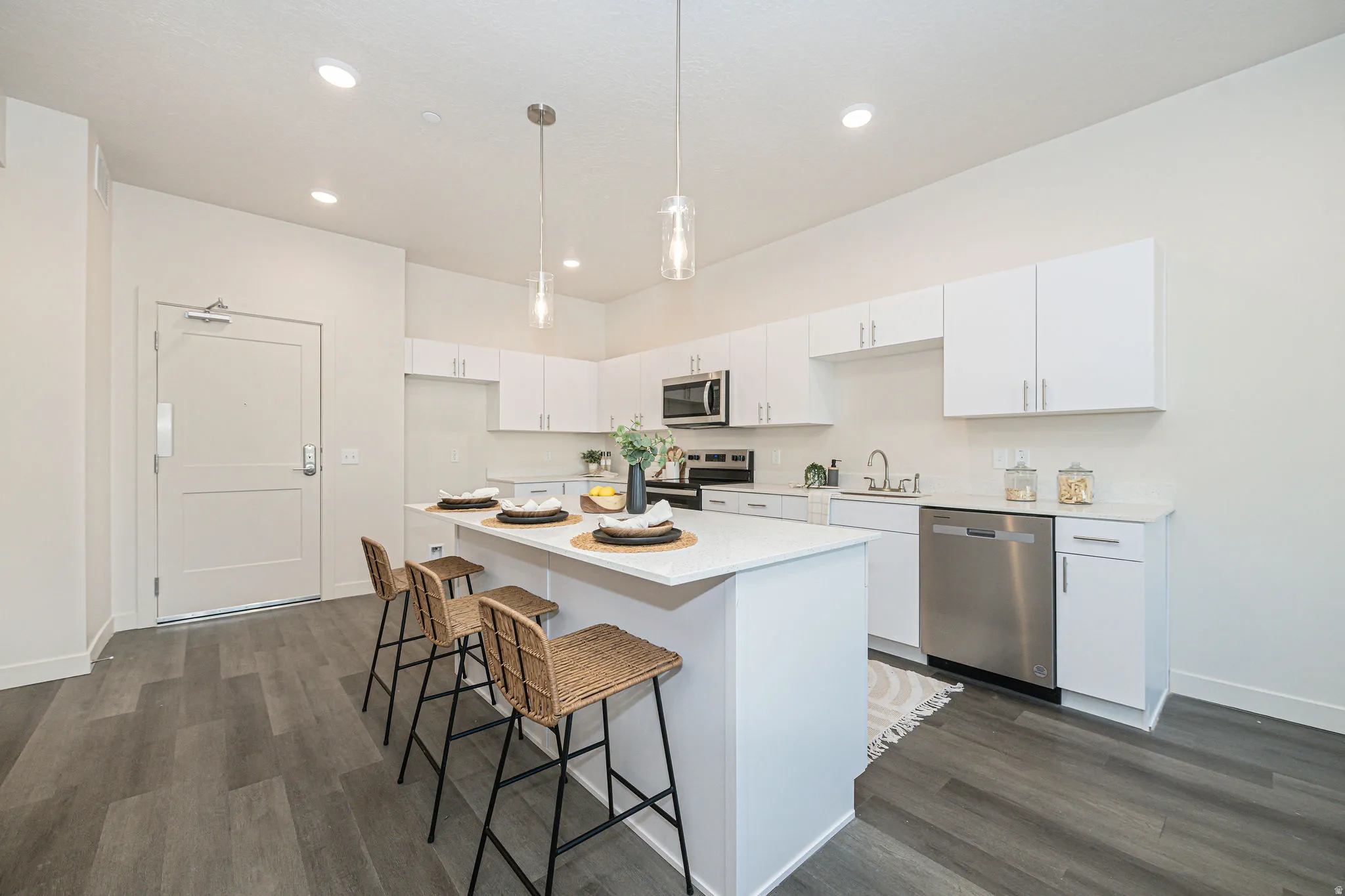 Kitchen featuring white cabinetry, appliances with stainless steel finishes, hanging light fixtures, a kitchen island, and dark wood-style flooring