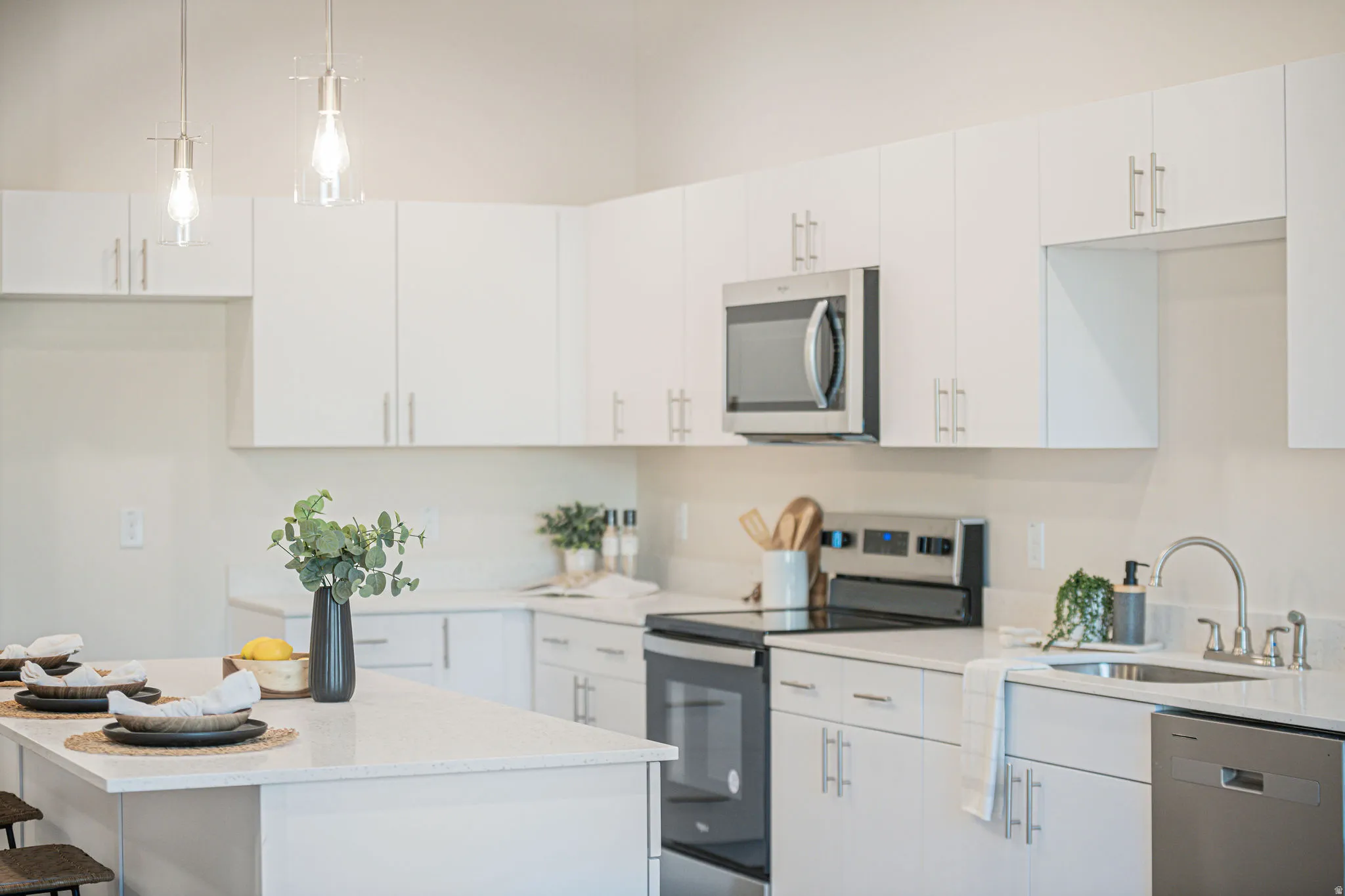 Kitchen featuring stainless steel appliances, a breakfast bar area, pendant lighting, white cabinets, and light stone counters