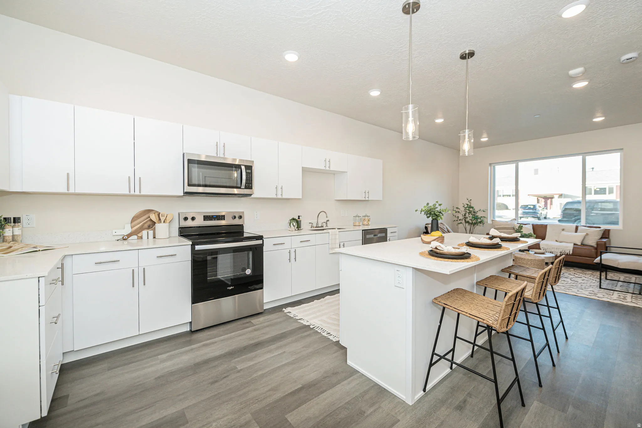 Kitchen with stainless steel appliances, white cabinets, pendant lighting, light wood finished floors, and a kitchen bar