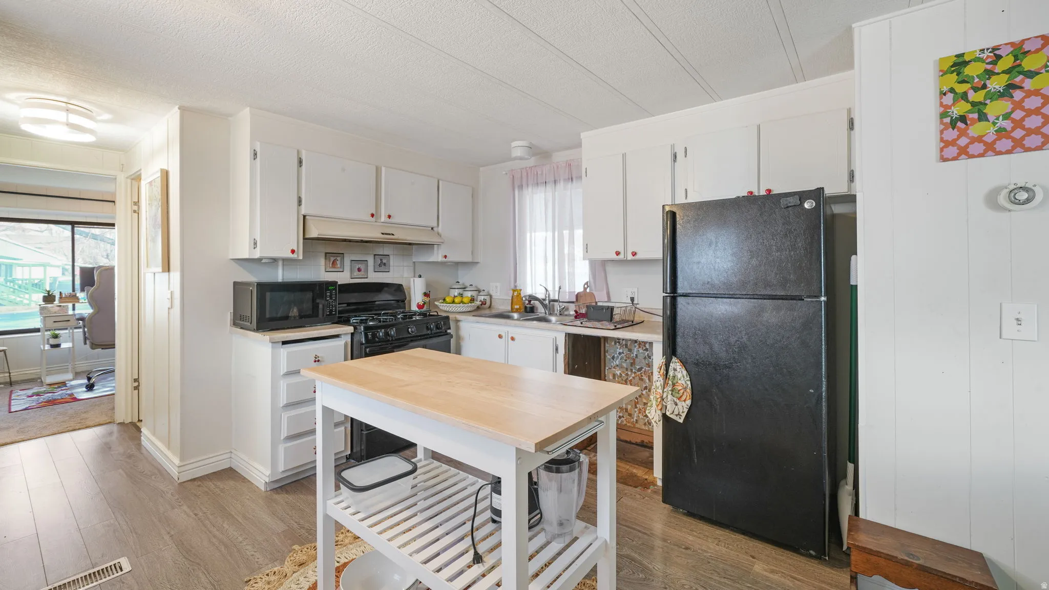 Kitchen featuring white cabinets, black appliances, light countertops, light wood-style flooring, and a textured ceiling