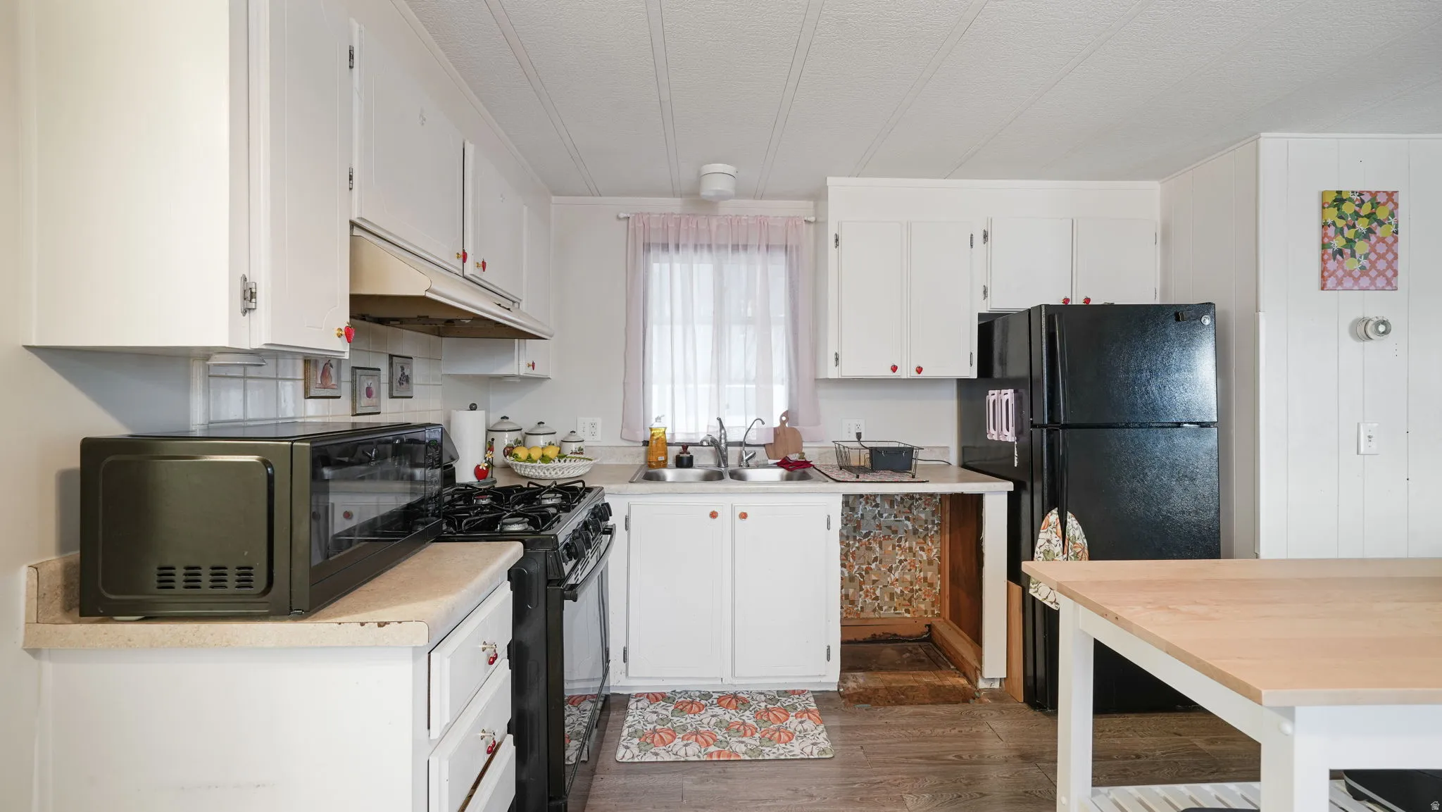 Kitchen with light countertops, black appliances, under cabinet range hood, white cabinets, and crown molding