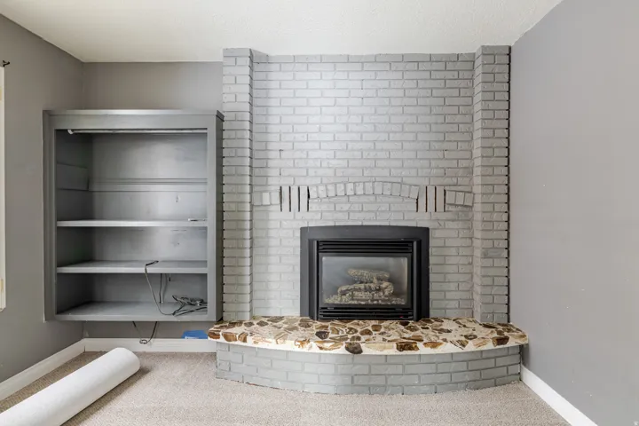 Detailed view of a brick fireplace, carpet flooring, and a textured ceiling
