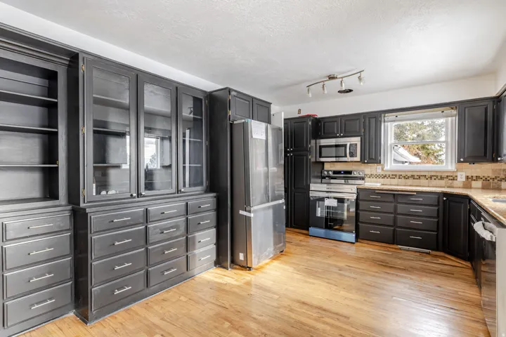 Kitchen featuring appliances with stainless steel finishes, glass insert cabinets, light wood-type flooring, a textured ceiling, and open shelves