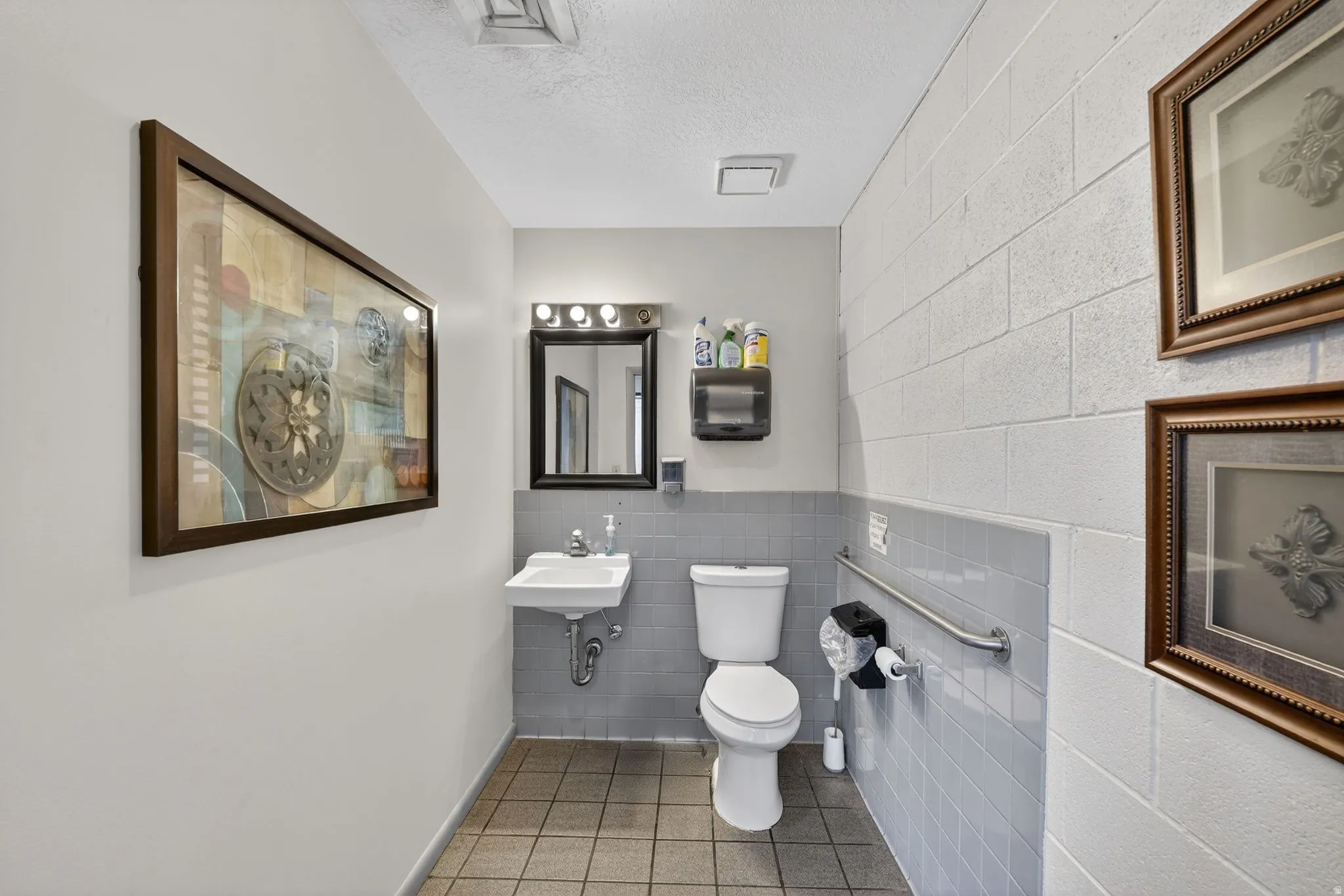 Half bath featuring tile walls, a textured ceiling, light tile patterned flooring, and wainscoting