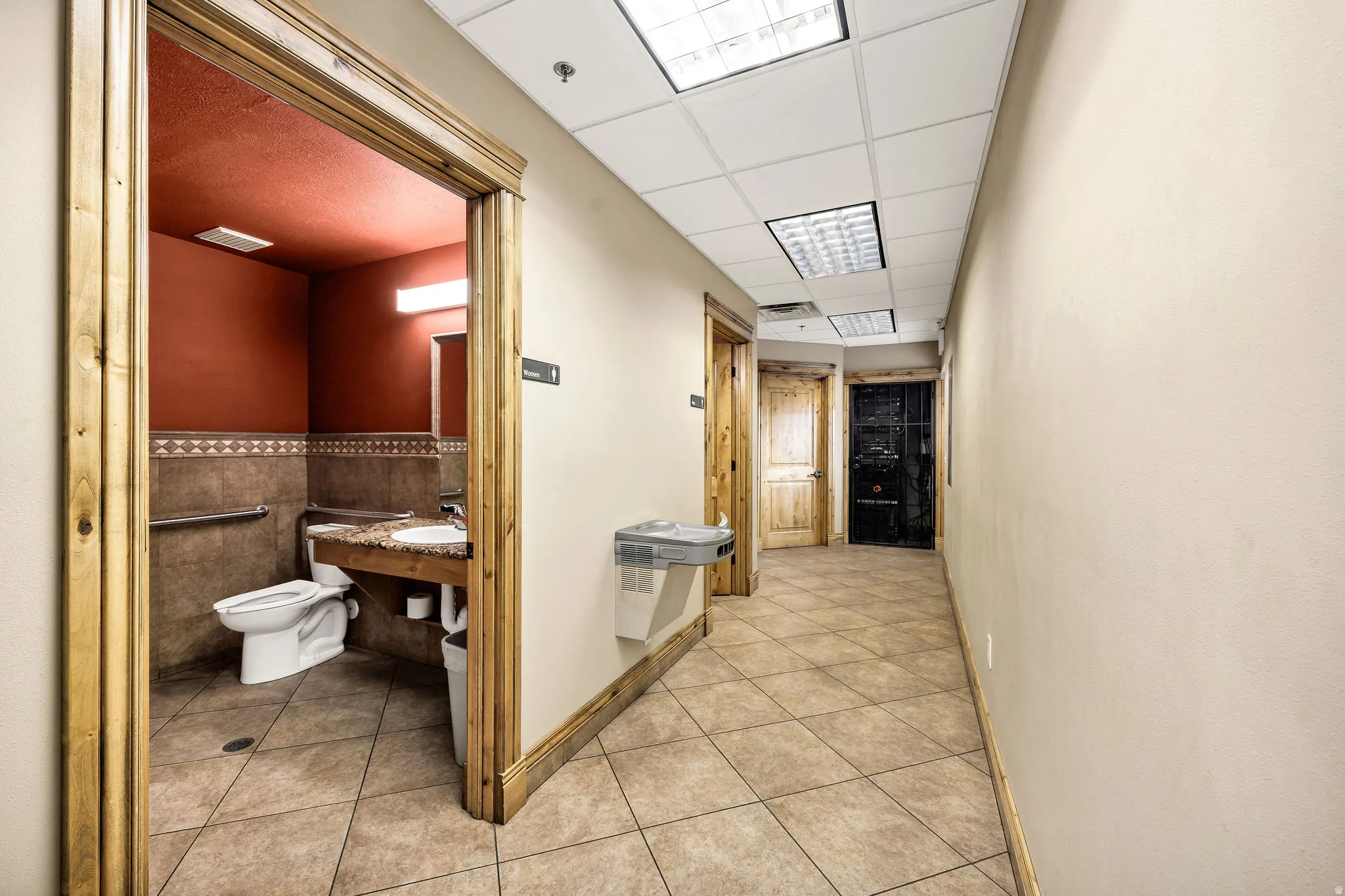 Corridor with light tile patterned floors, a paneled ceiling, and tile walls