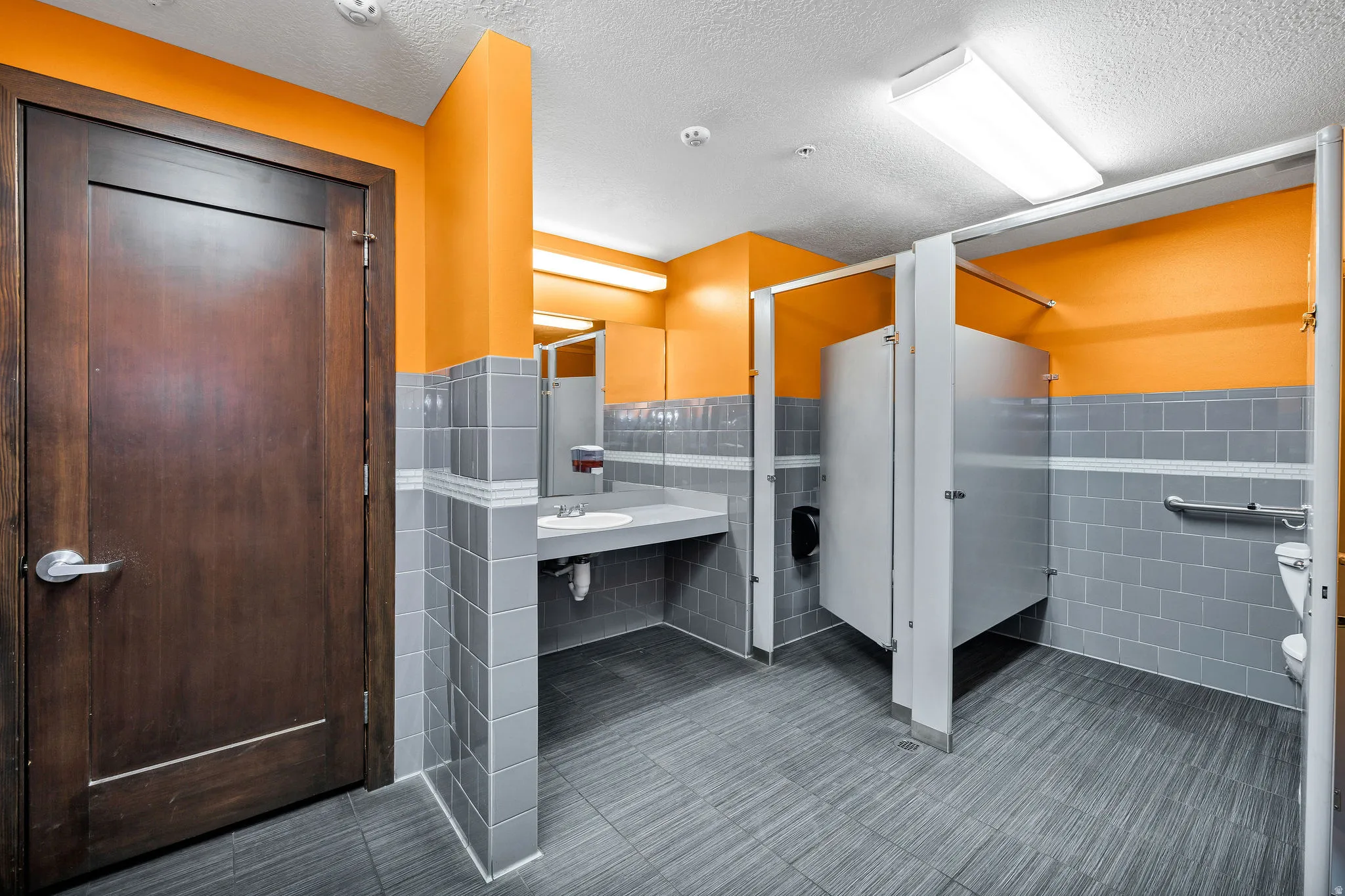 Bathroom featuring a wainscoted wall, tile walls, a stall shower, and a textured ceiling