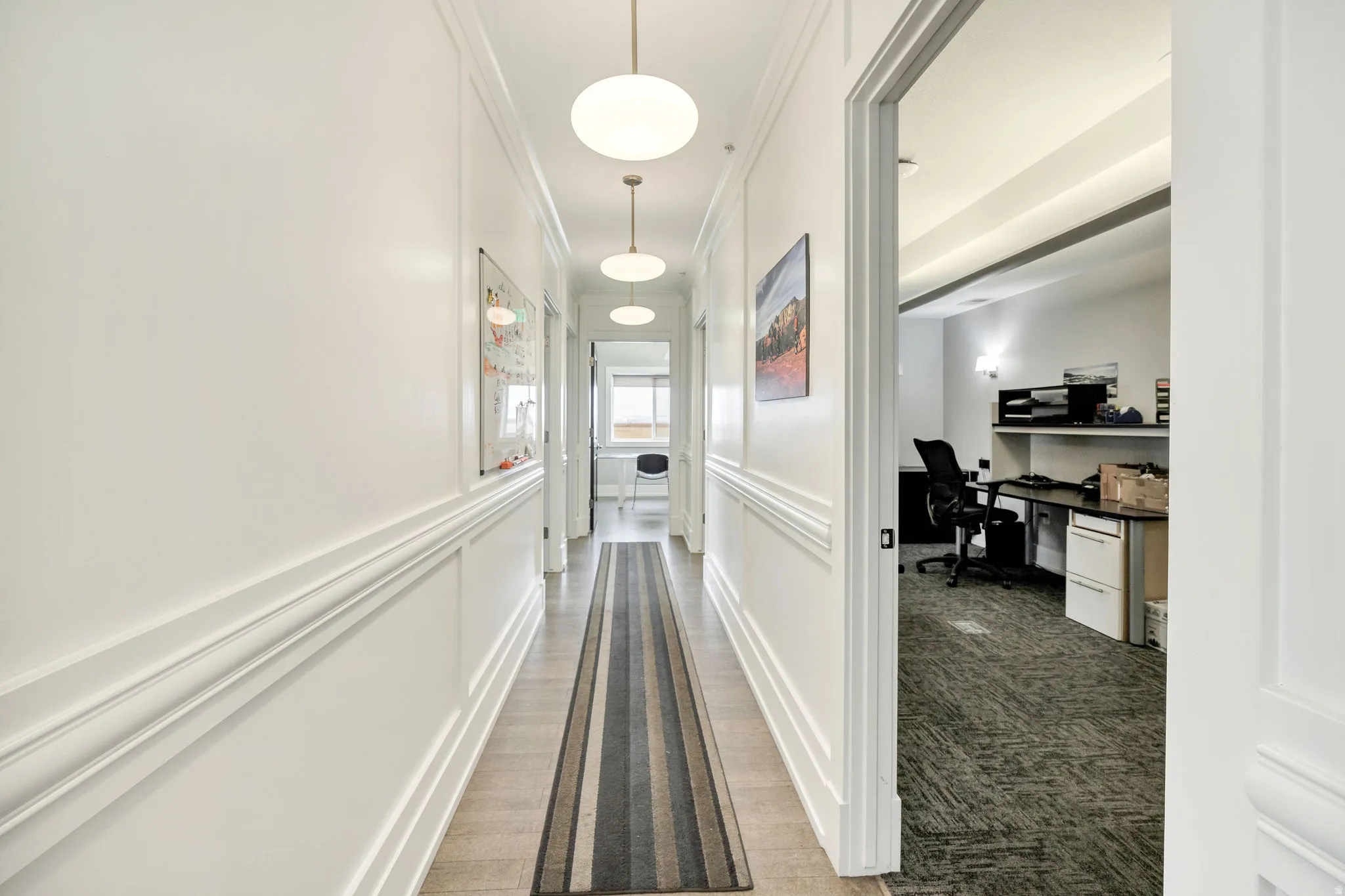 Hallway featuring an office area, ornamental molding, a decorative wall, and wainscoting