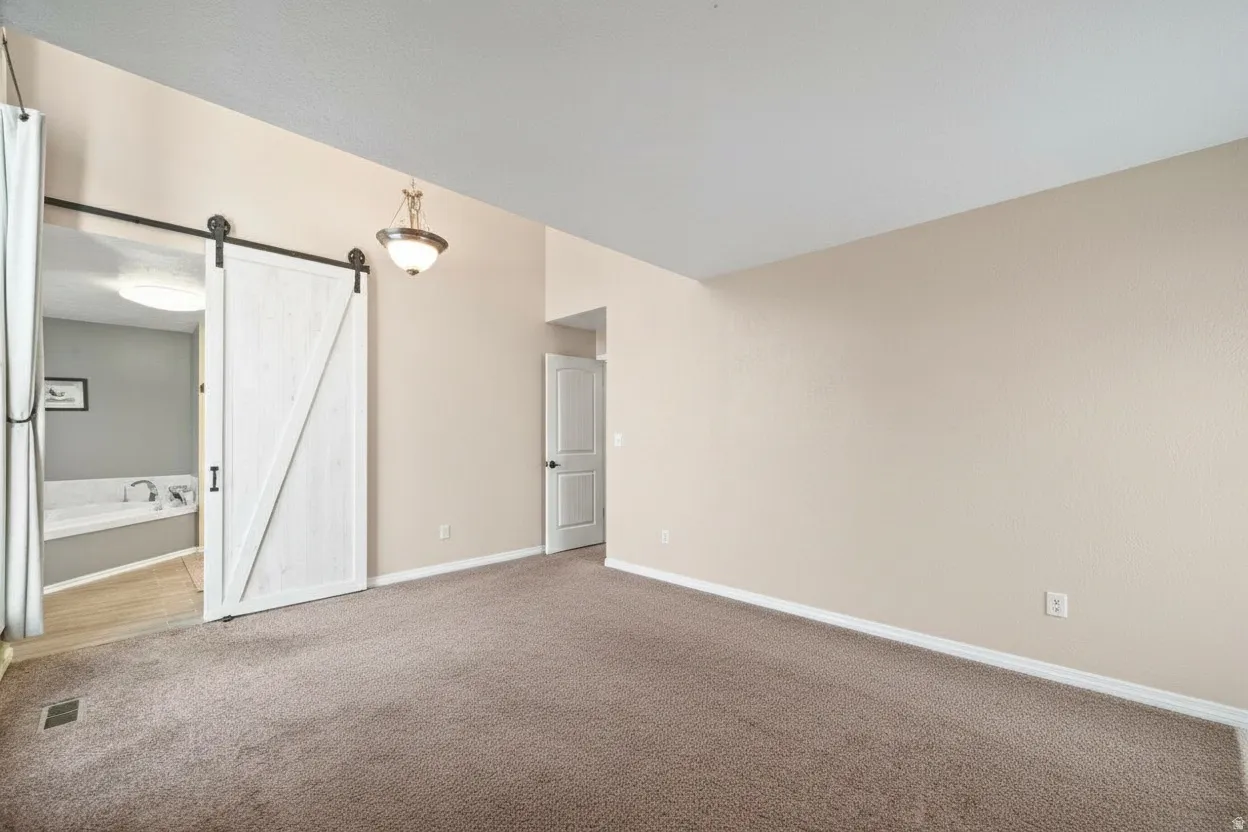 Neutral-toned room featuring a white barn door, a built-in soaking tub, sloped ceiling, and a dome light fixture