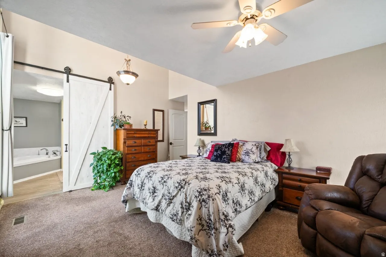 Carpeted bedroom with a barn door, a ceiling fan, and ensuite bathroom