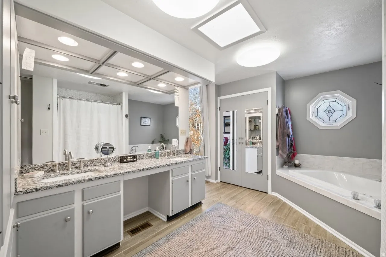 Bathroom with curtained shower, double vanity, light wood-type flooring, and a bath