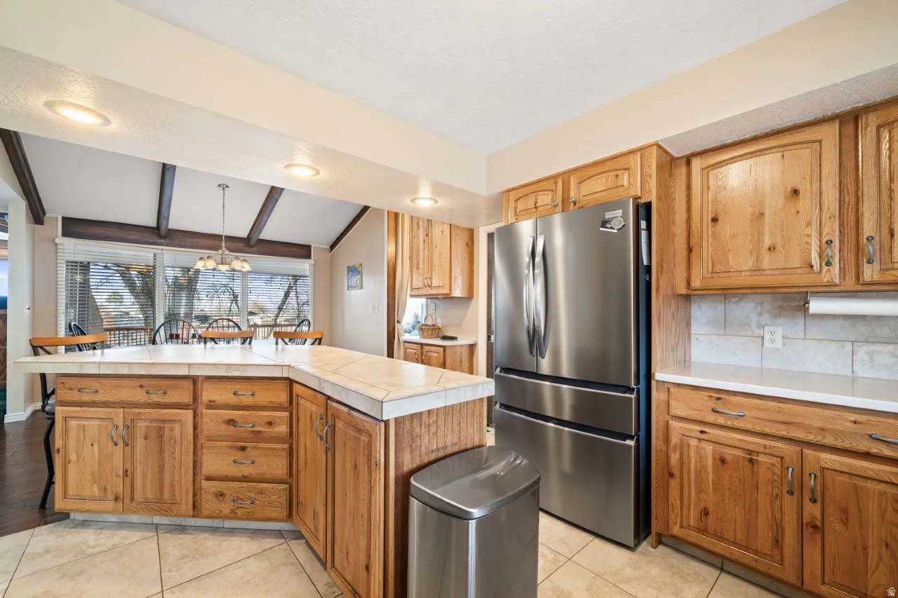 Kitchen featuring hanging light fixtures, freestanding refrigerator, backsplash, a chandelier, and light tile patterned floors