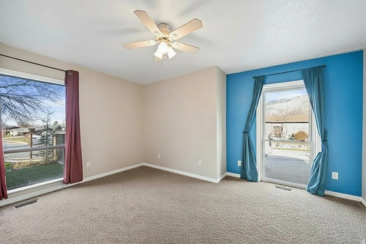 Spacious room featuring carpeted flooring, a ceiling fan with integrated lighting, and a large window with street views