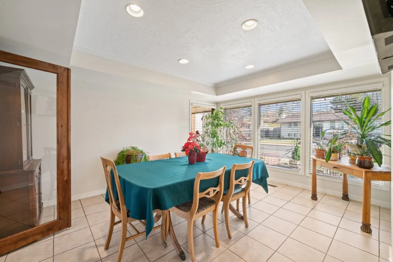 Dining room with a textured ceiling, ornamental molding, light tile patterned flooring, a tray ceiling, and recessed lighting