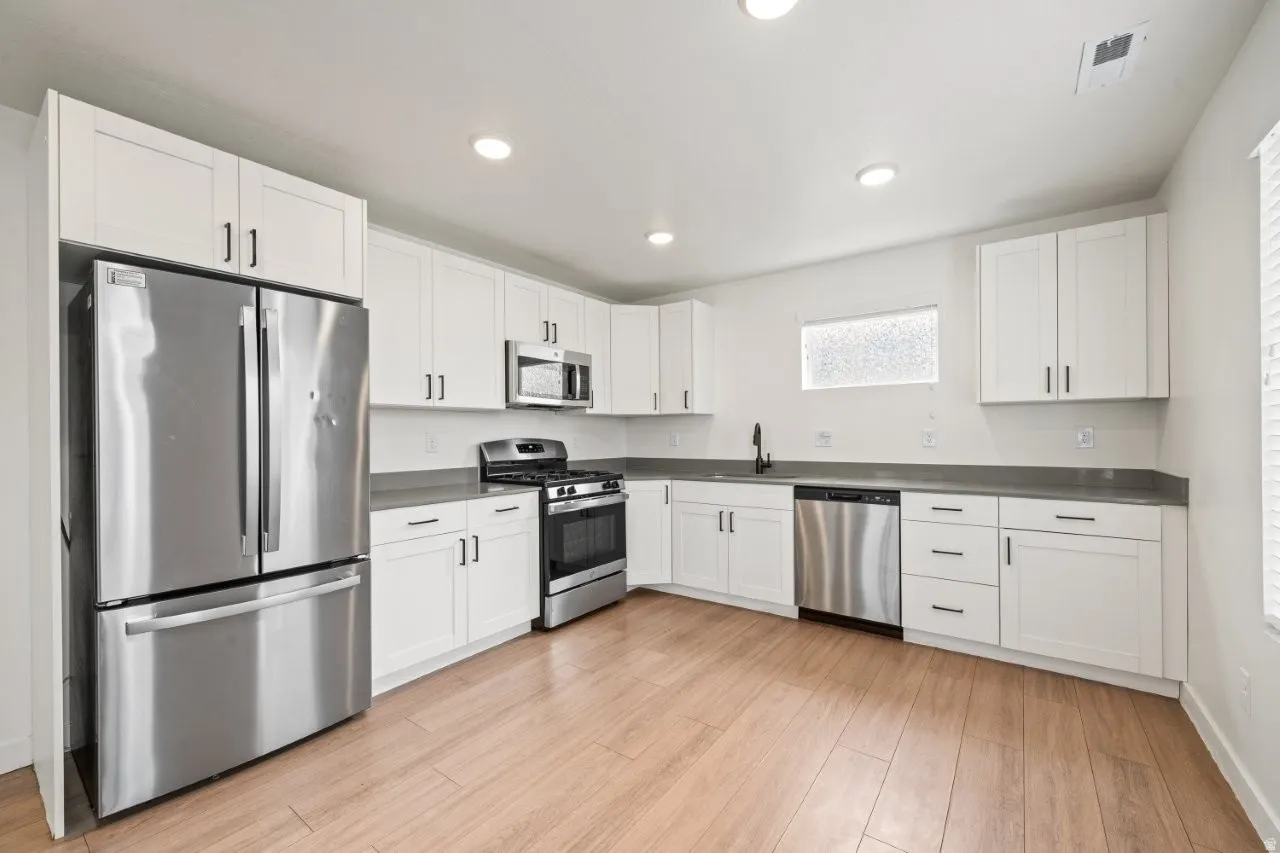 Kitchen featuring appliances with stainless steel finishes, white cabinetry, light wood-style flooring, recessed lighting, and dark countertops