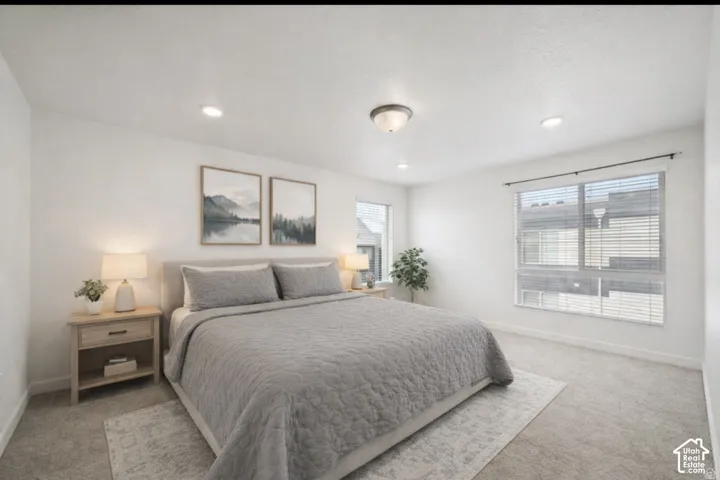 Primary bedroom with two windows, natural light, featuring light colored carpet and recessed lighting.  Virtually staged.