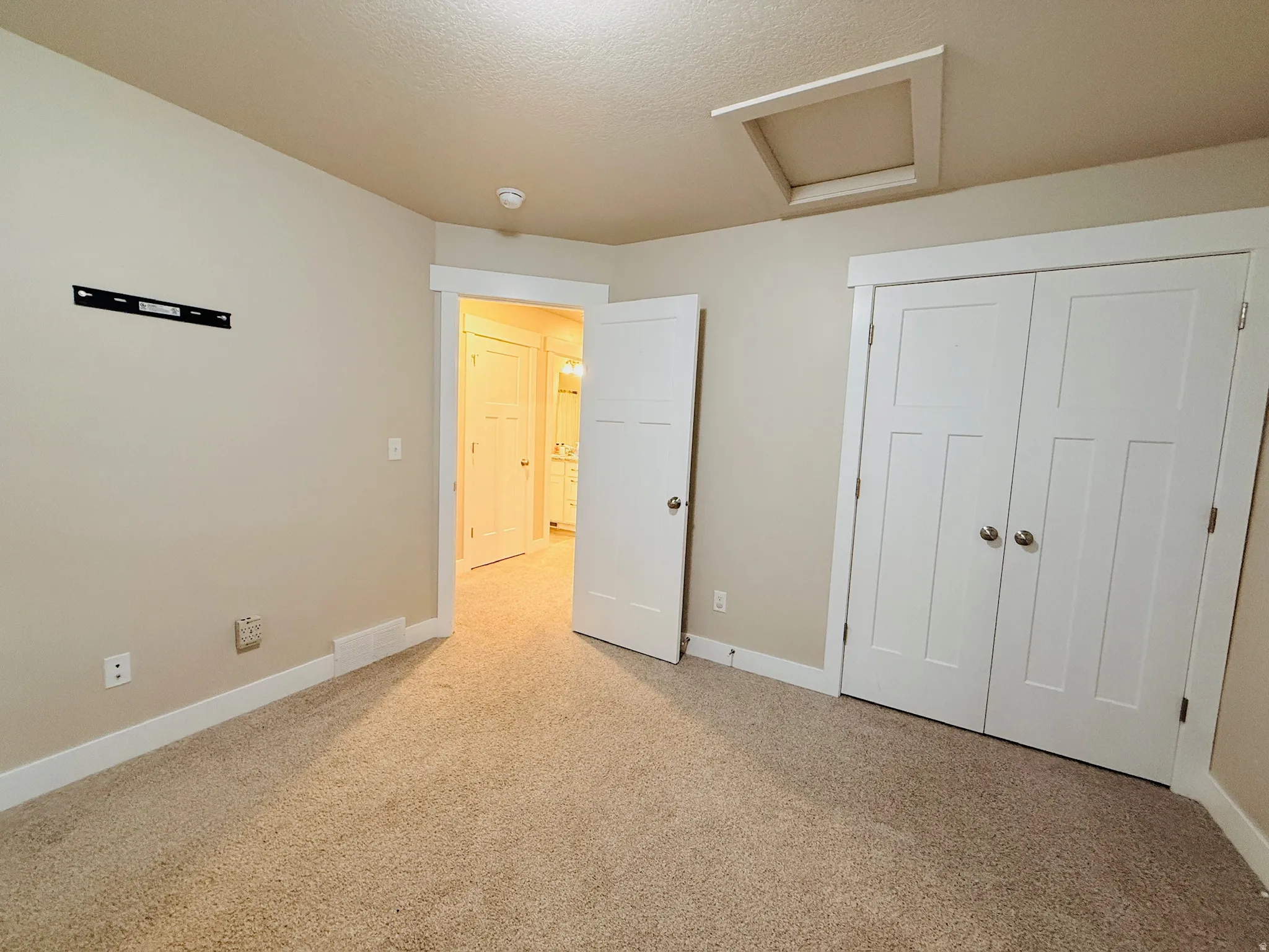 Unfurnished bedroom featuring attic access, light carpet, a closet, and a textured ceiling