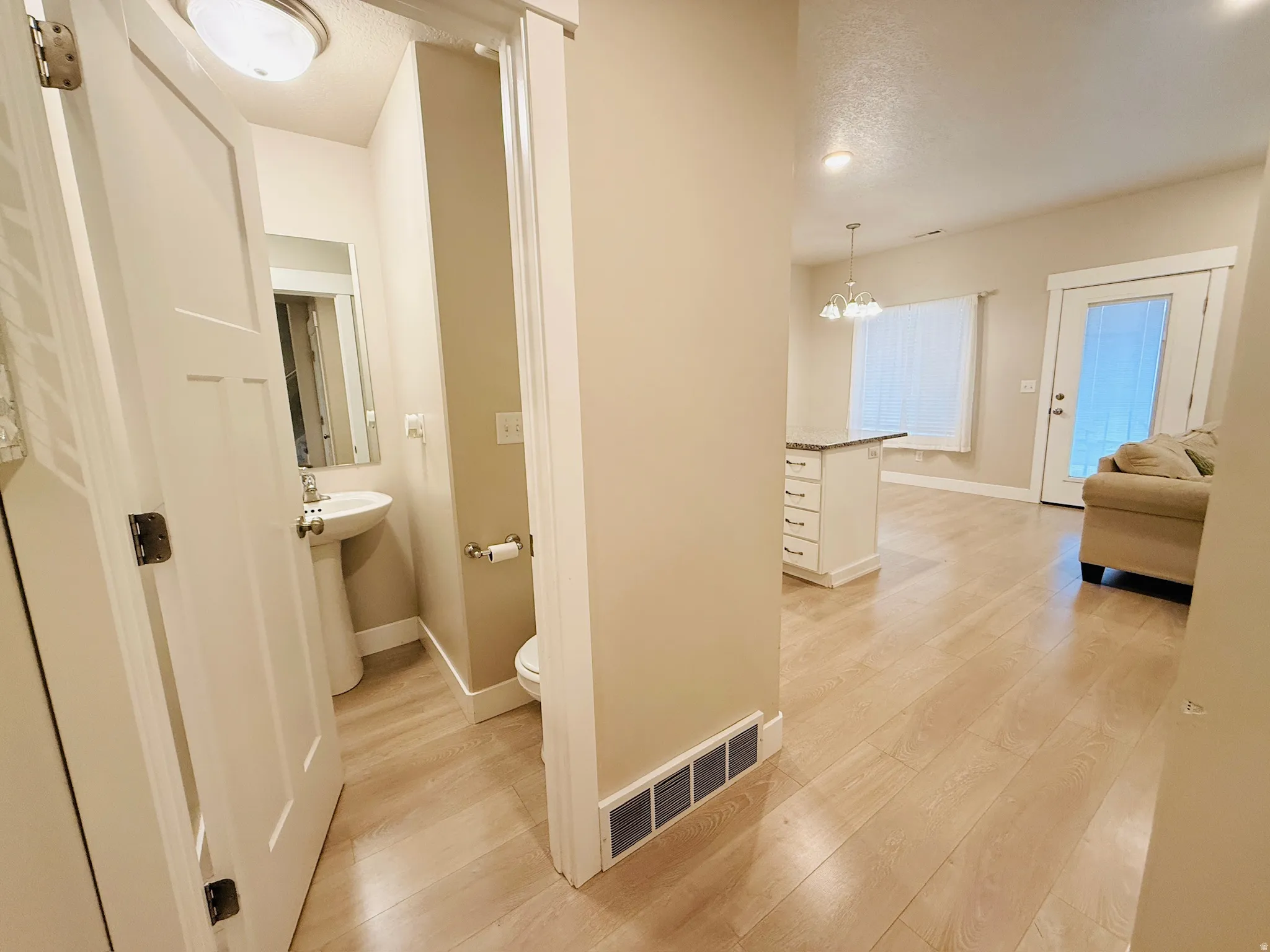 Corridor featuring light wood-style floors, a textured ceiling, and a chandelier