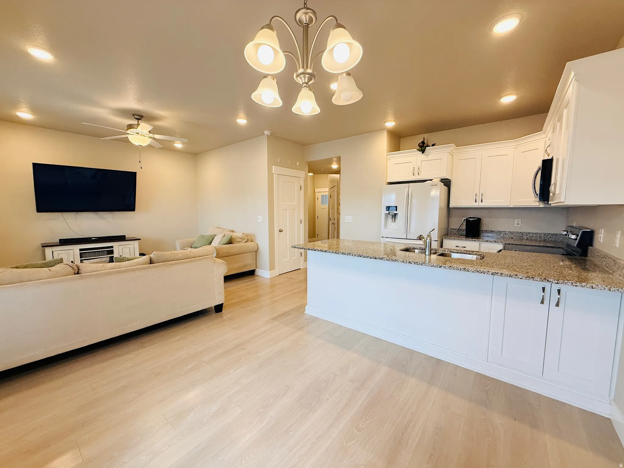 Kitchen featuring open floor plan, hanging light fixtures, light stone countertops, recessed lighting, and white cabinets