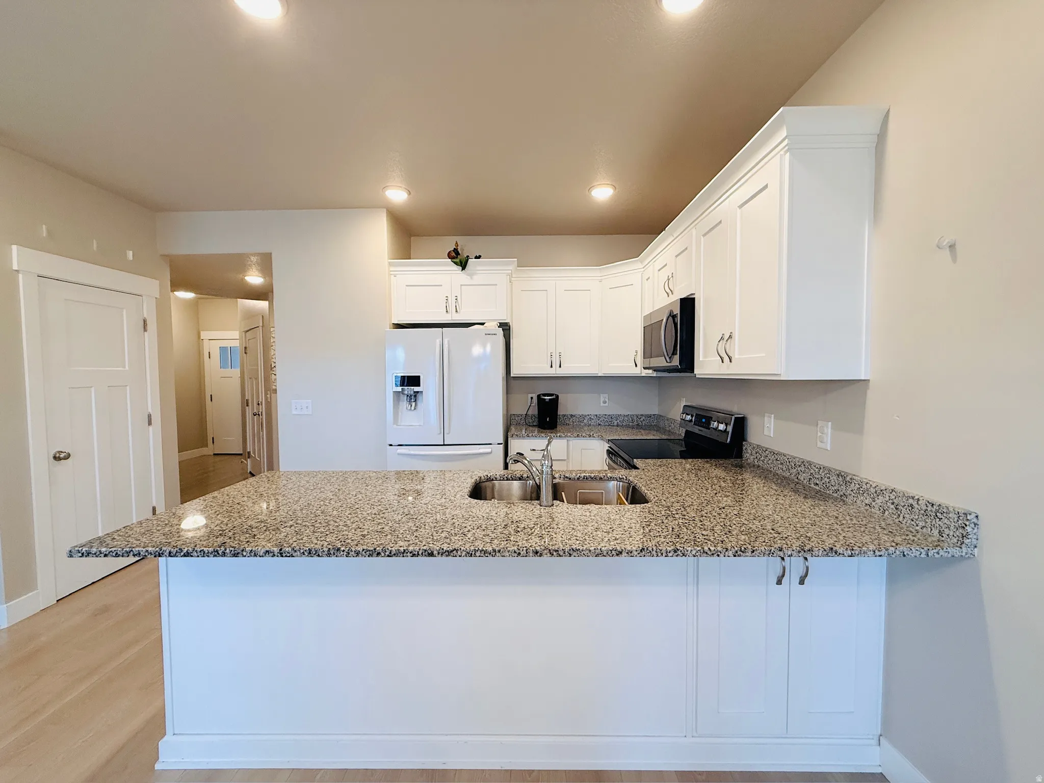 Kitchen featuring white cabinets, white refrigerator with ice dispenser, dark stone countertops, a peninsula, and black range with electric stovetop