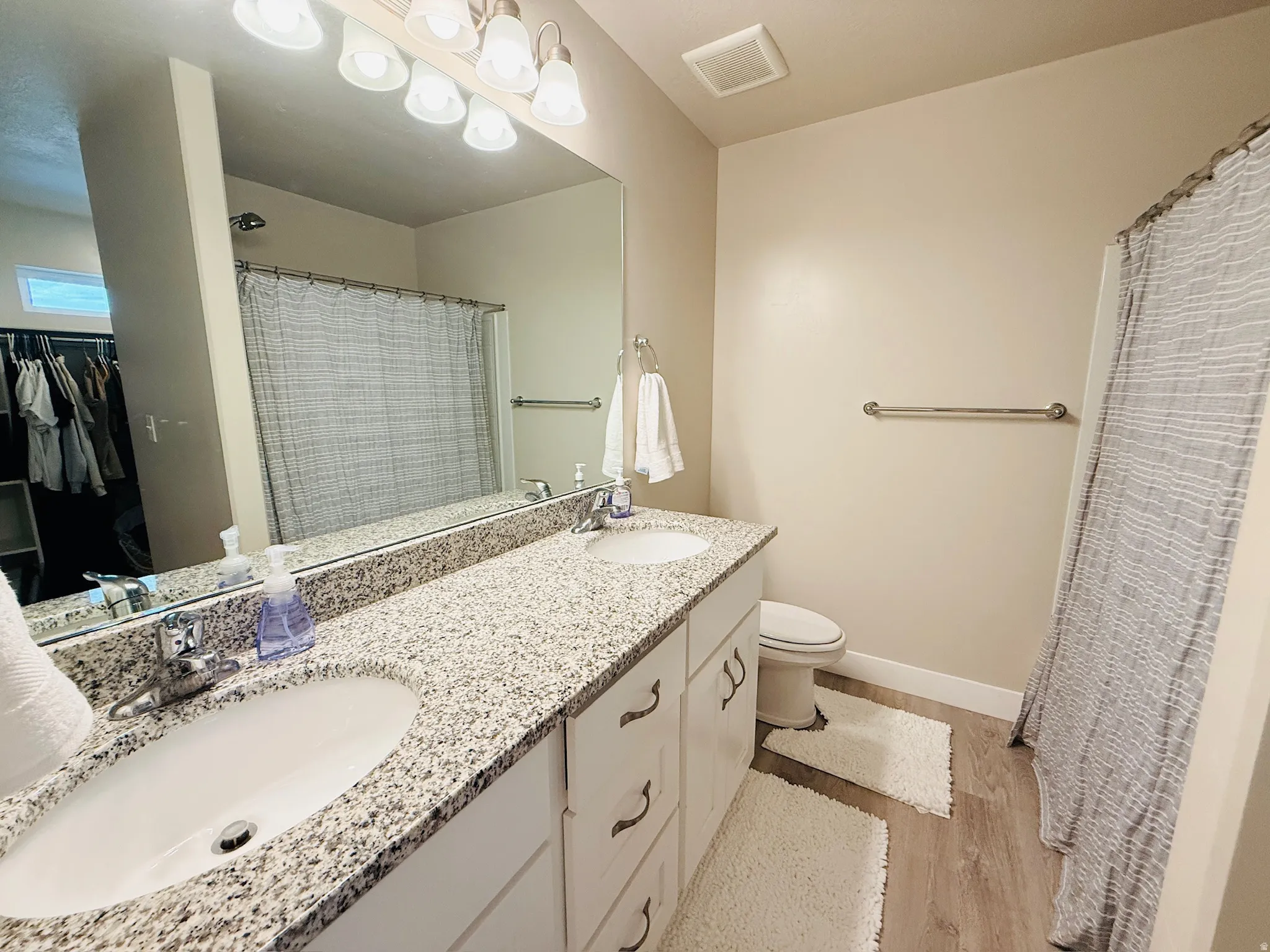 Full bath with double vanity, a shower with shower curtain, light wood-style floors, and a spacious closet