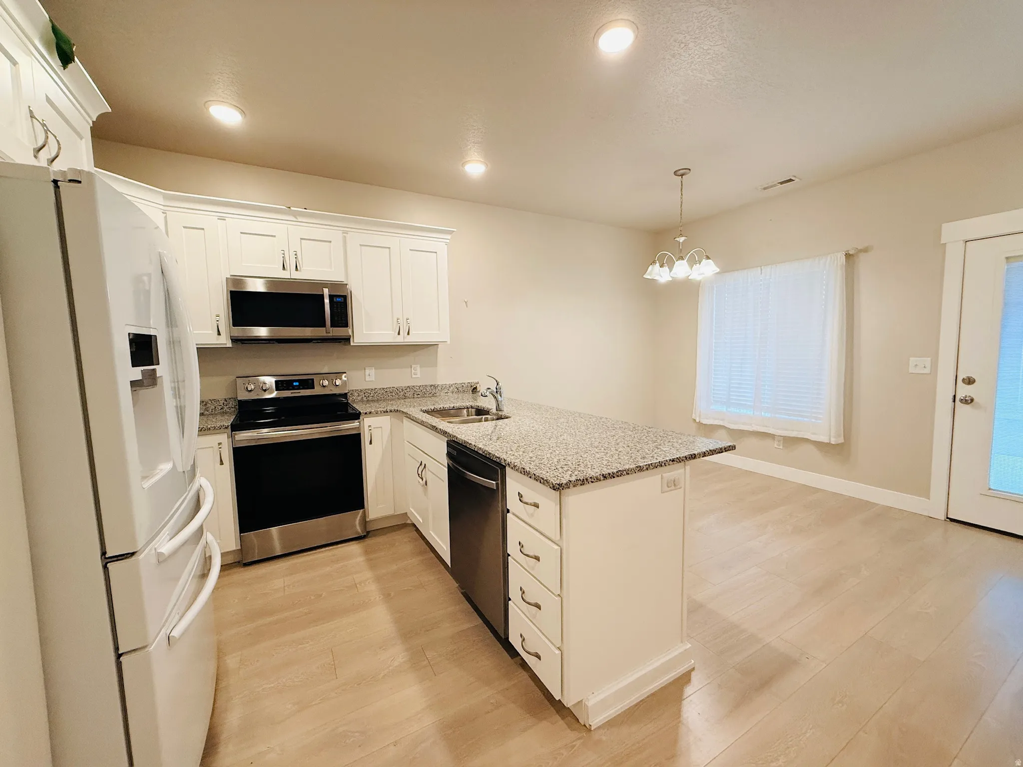 Kitchen featuring stainless steel appliances, light stone countertops, a peninsula, white cabinets, and pendant lighting