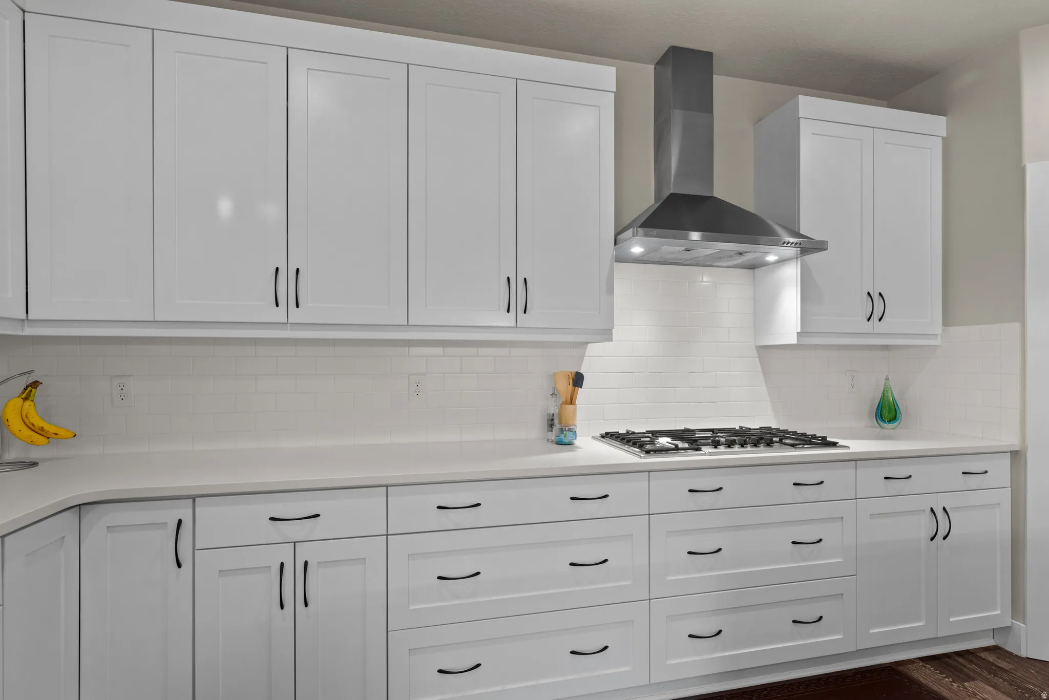 Kitchen featuring white cabinets, wall chimney exhaust hood, tasteful backsplash, and light stone counters