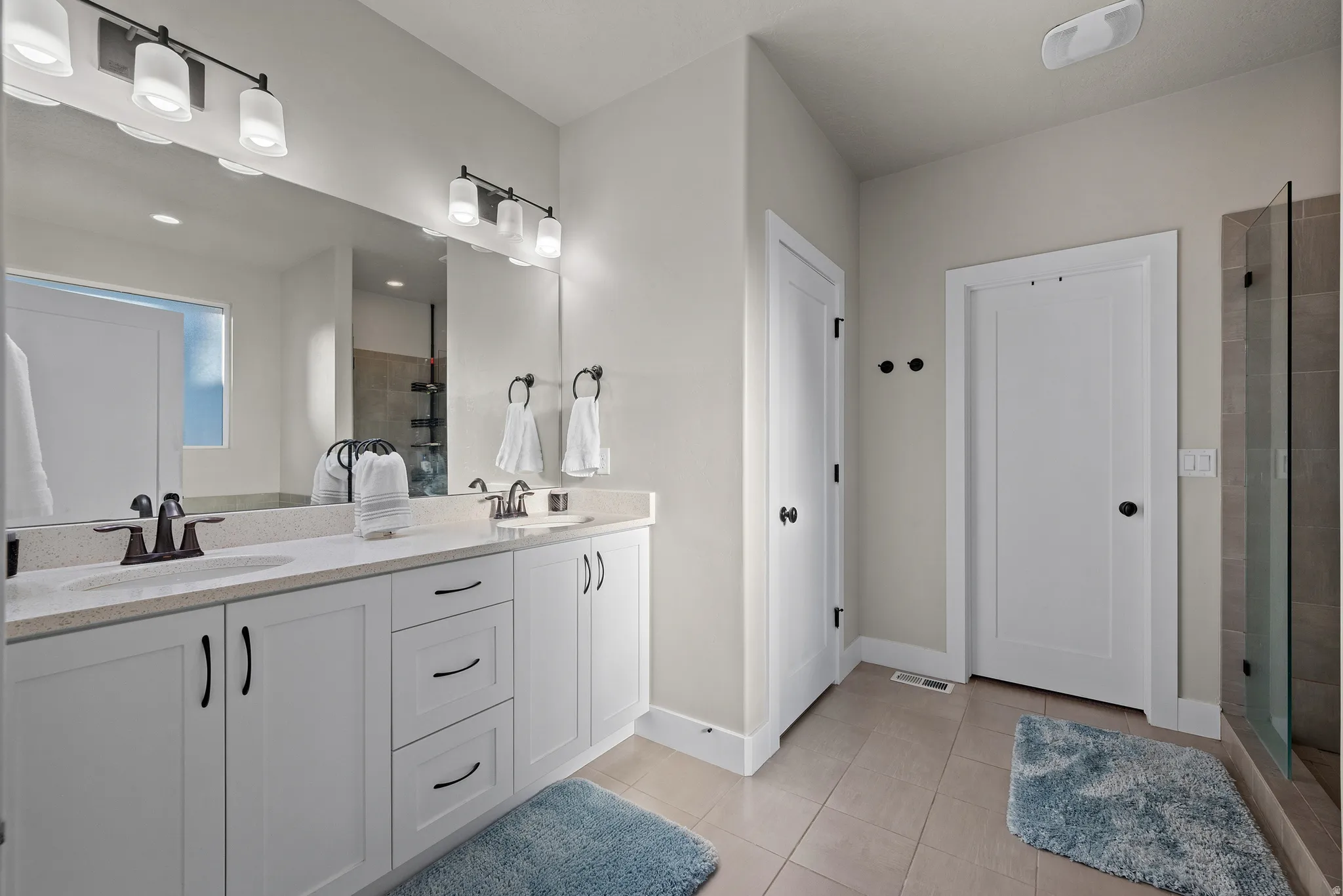 Bathroom with double vanity, light tile patterned floors, and a stall shower