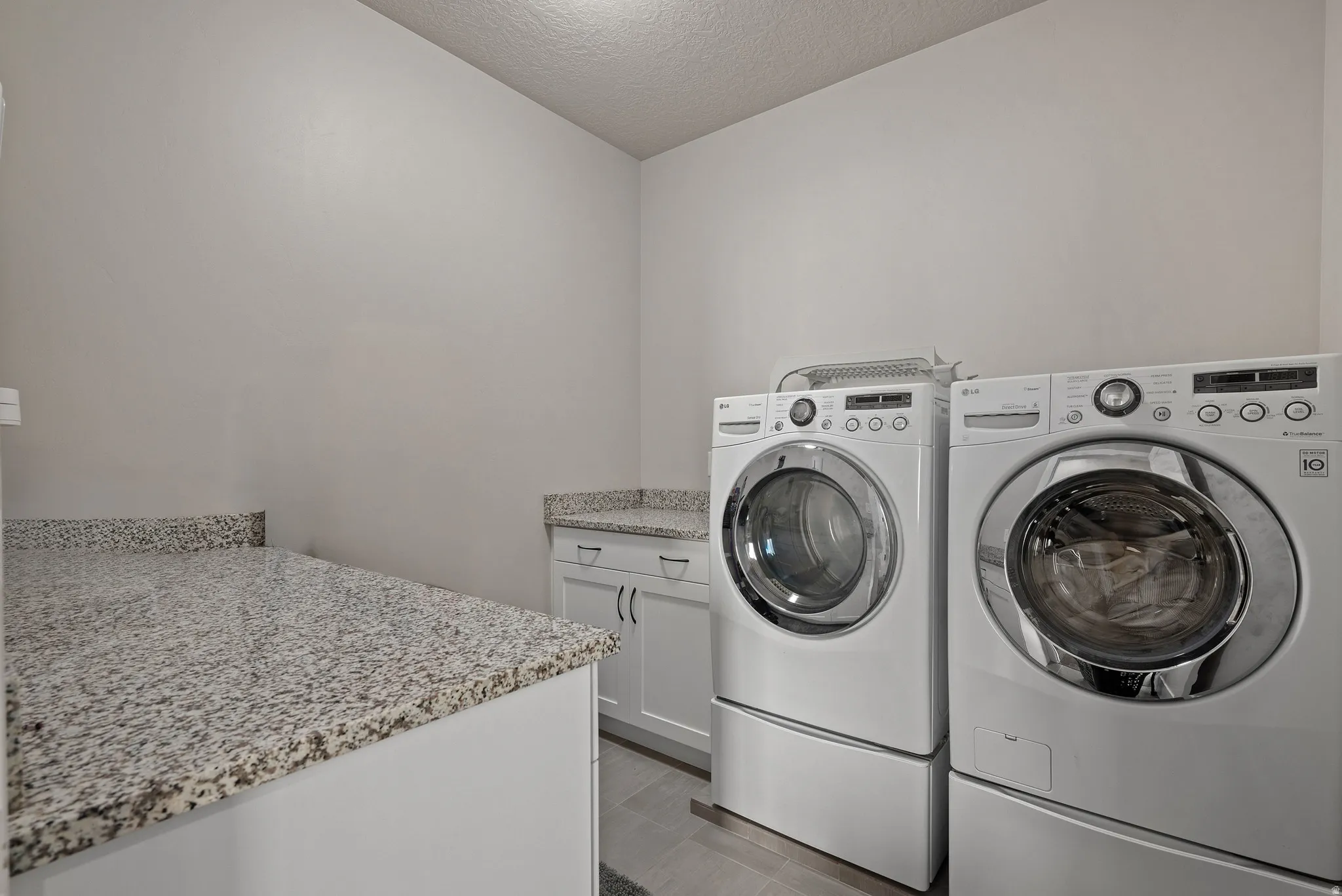 Laundry room featuring cabinet space, a textured ceiling, and washing machine and clothes dryer