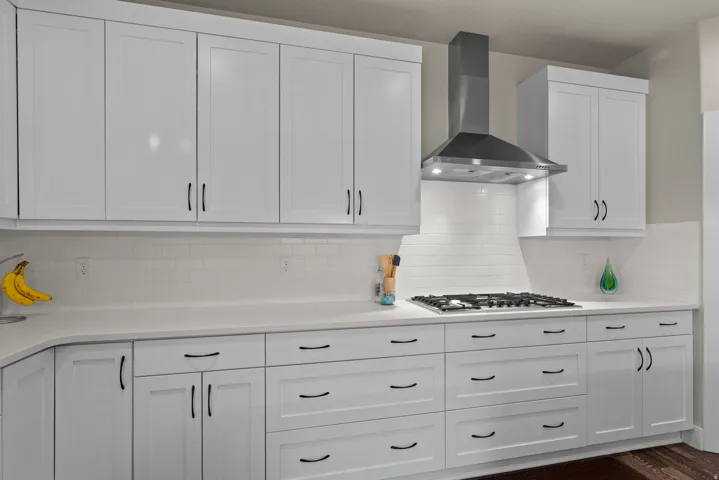 Kitchen featuring white cabinets, wall chimney exhaust hood, tasteful backsplash, and light stone counters