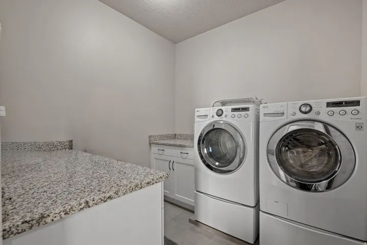 Laundry room featuring cabinet space, a textured ceiling, and washing machine and clothes dryer