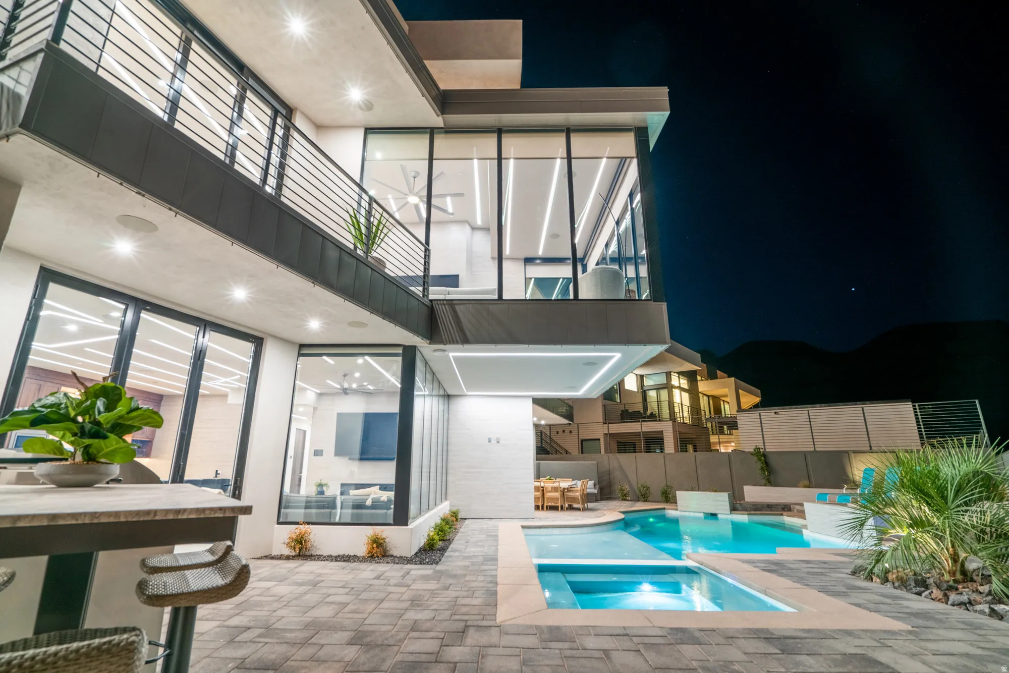 Pool at night with a balcony, a patio, a pool with connected hot tub, and outdoor dining space