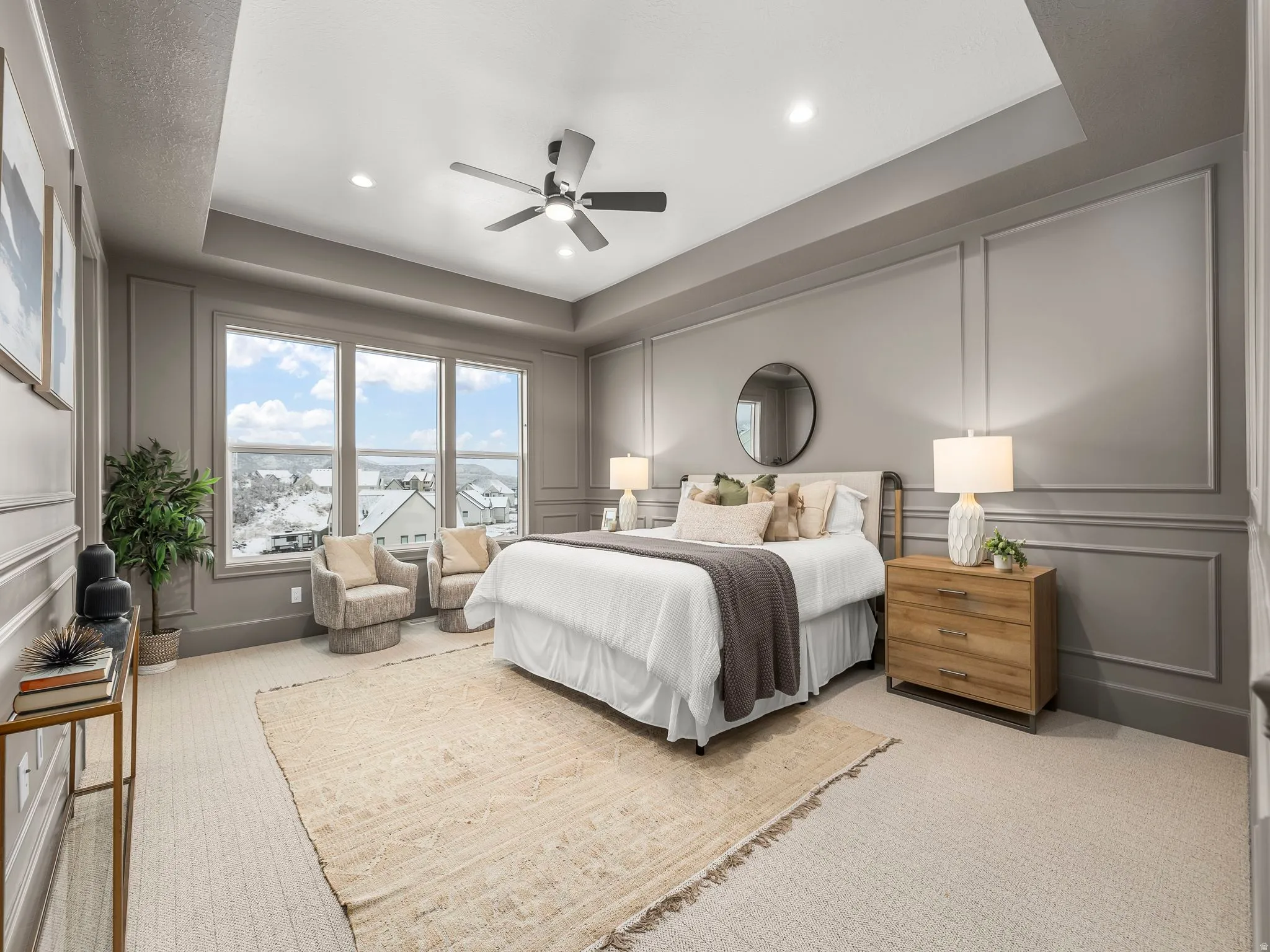 Bedroom with a decorative wall, a tray ceiling, a ceiling fan, light carpet, and a water view