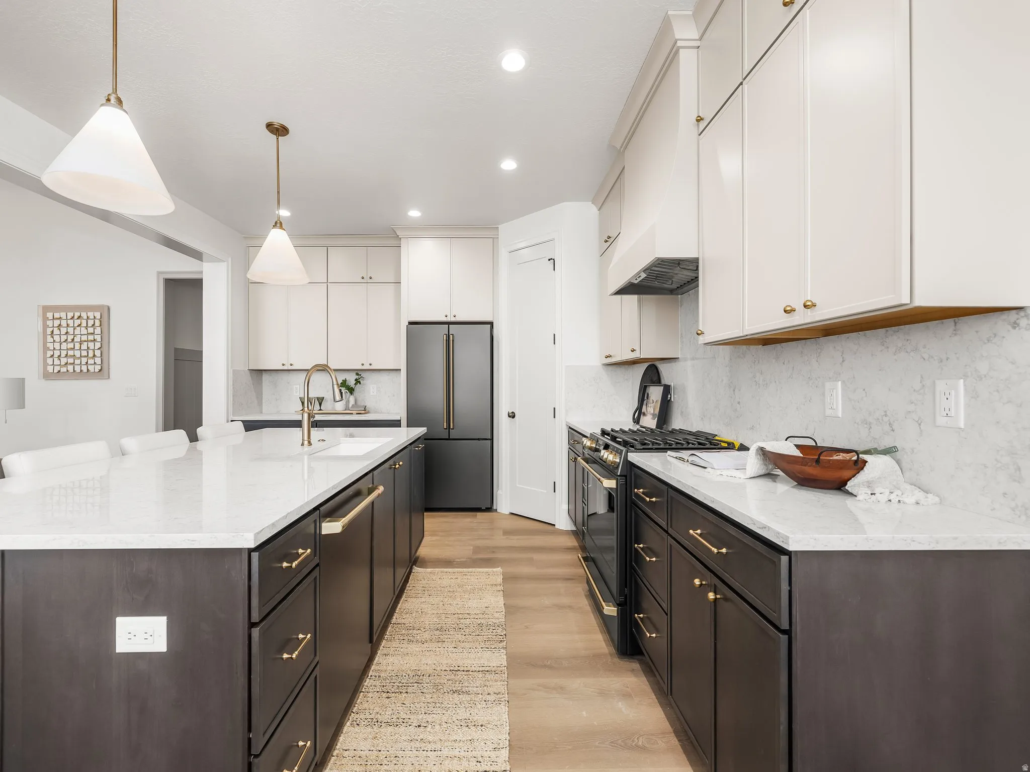 Kitchen featuring appliances with stainless steel finishes, pendant lighting, light stone countertops, an island with sink, and light wood-style floors