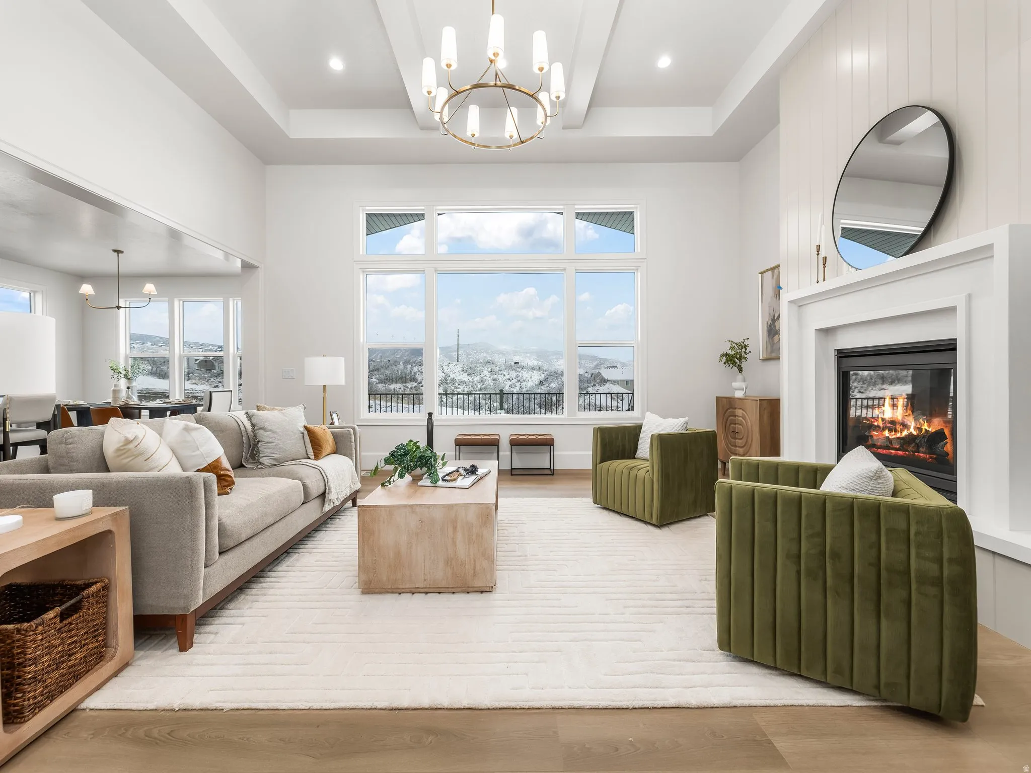 Living area with a chandelier, a towering ceiling, a glass covered fireplace, wood finished floors, and beamed ceiling
