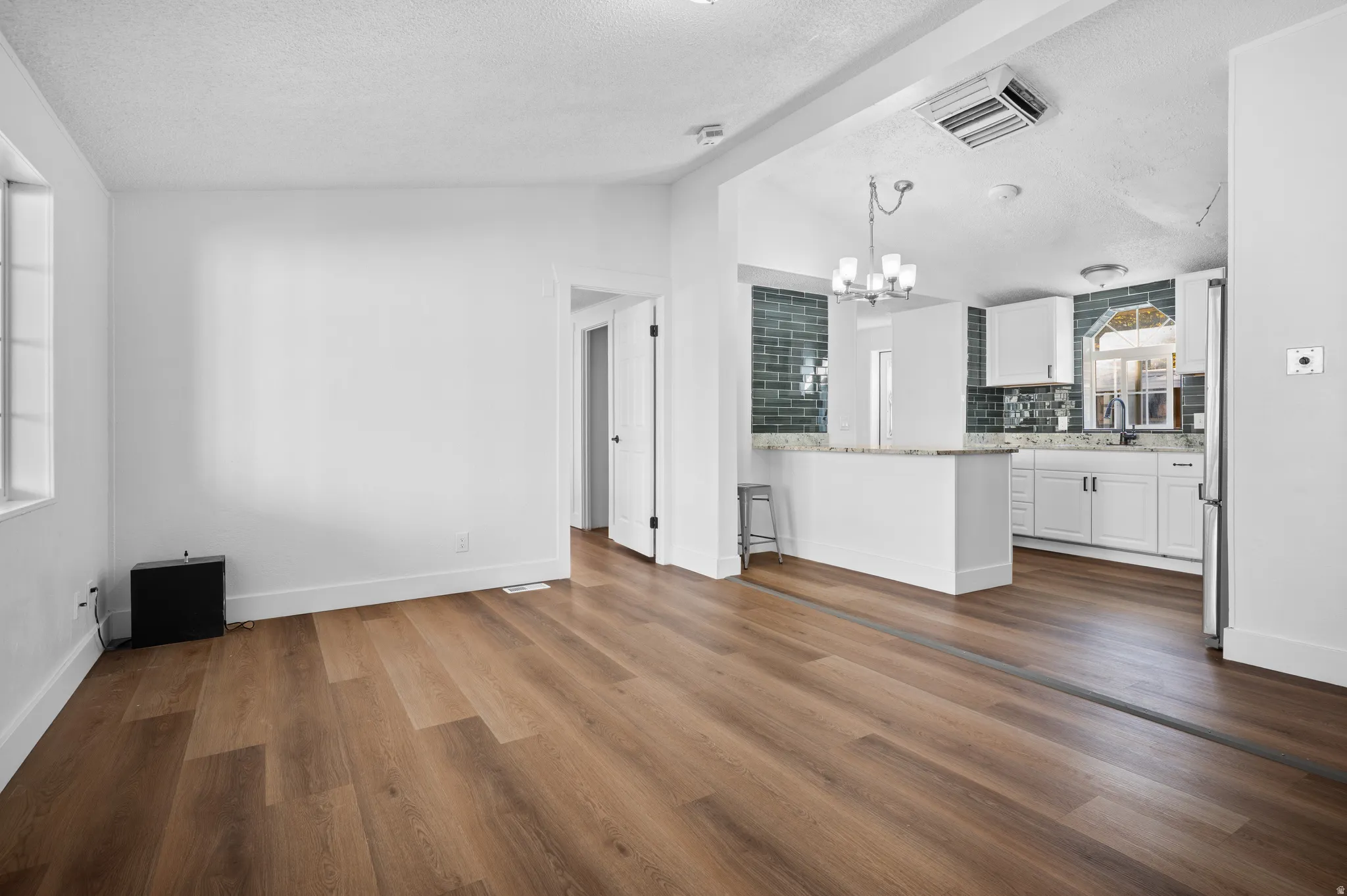 Unfurnished living room with vaulted ceiling, dark wood finished floors, a chandelier, and a textured ceiling