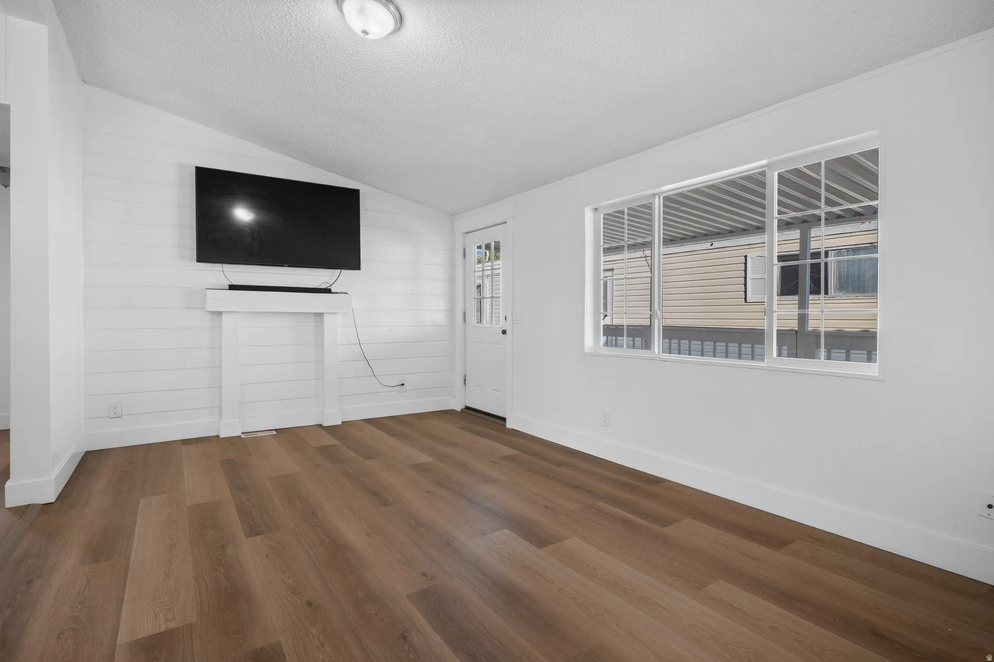Unfurnished living room with vaulted ceiling, a textured ceiling, and dark wood finished floors