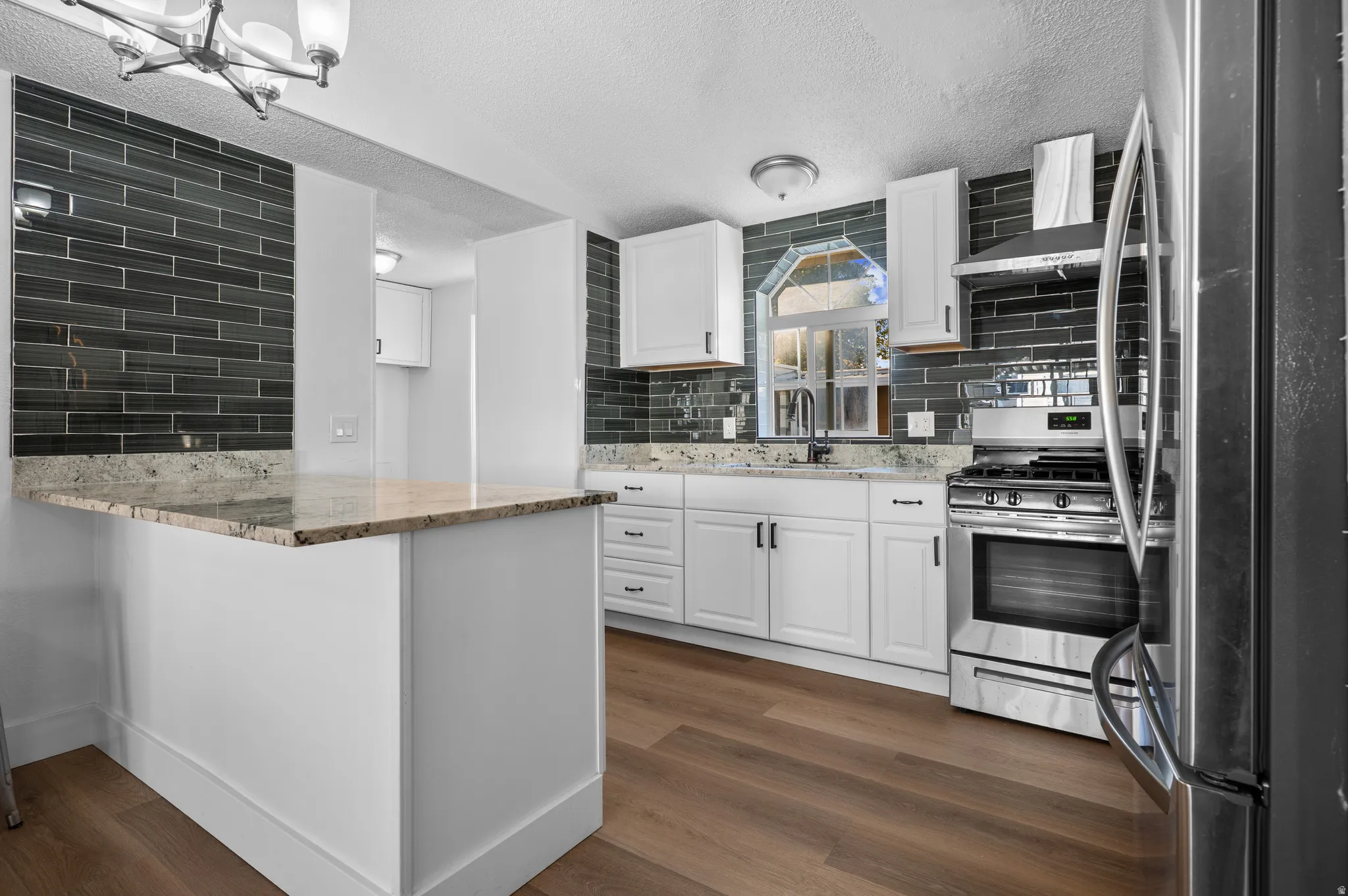 Kitchen with appliances with stainless steel finishes, white cabinetry, light stone counters, wall chimney range hood, and a textured ceiling