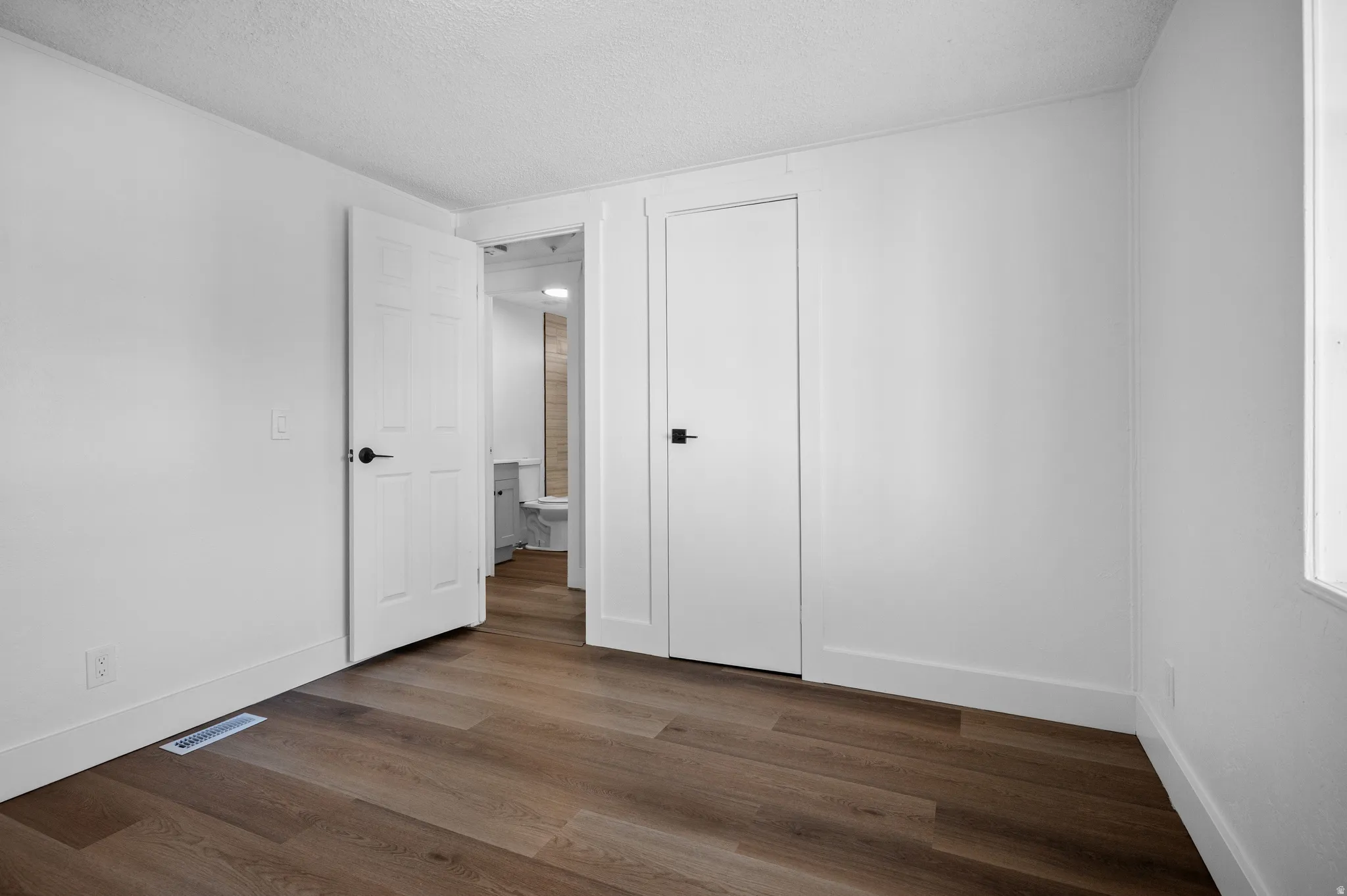 Unfurnished bedroom with dark wood-style flooring, a textured ceiling, and a closet