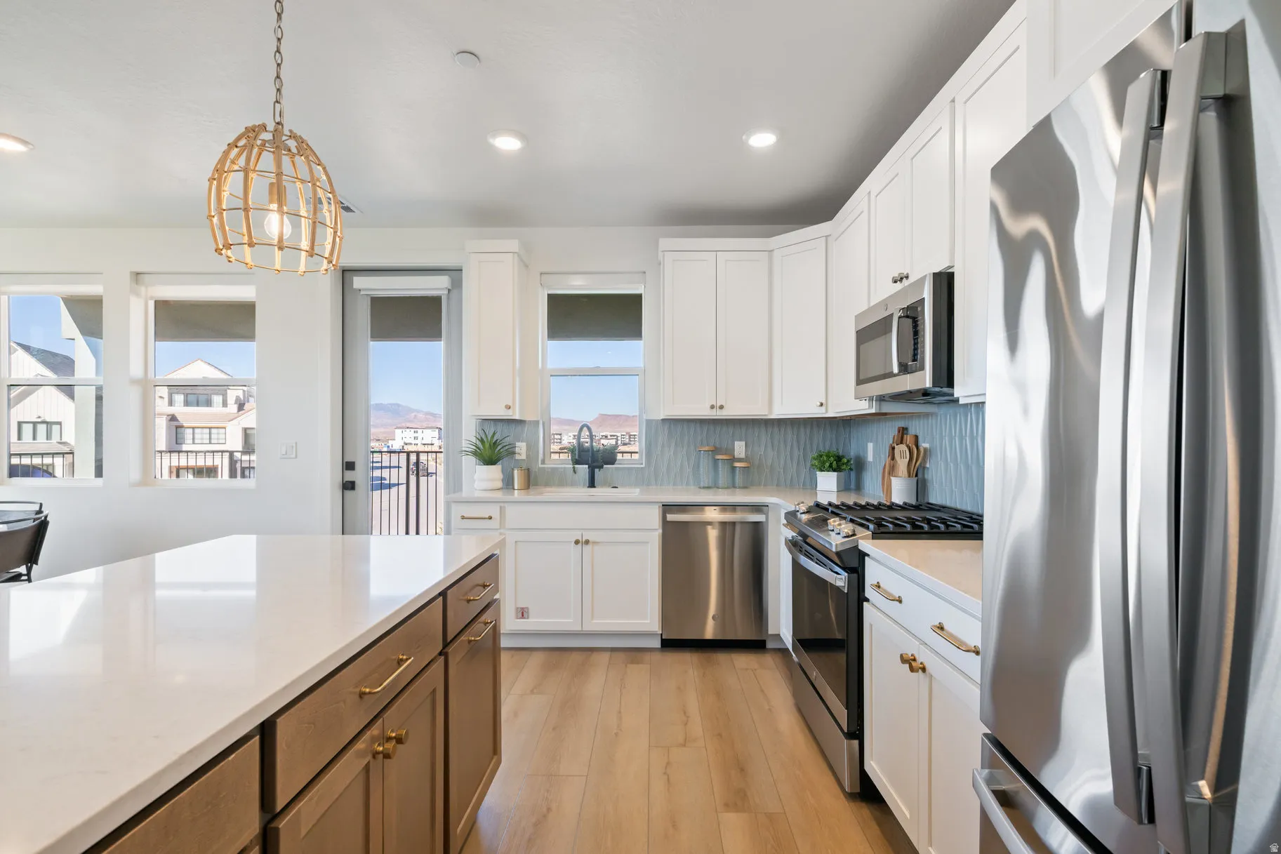 Two tone kitchen with stainless steel appliances, light wood-type flooring, decorative light fixtures, dual tone cabinets, and light stone counters