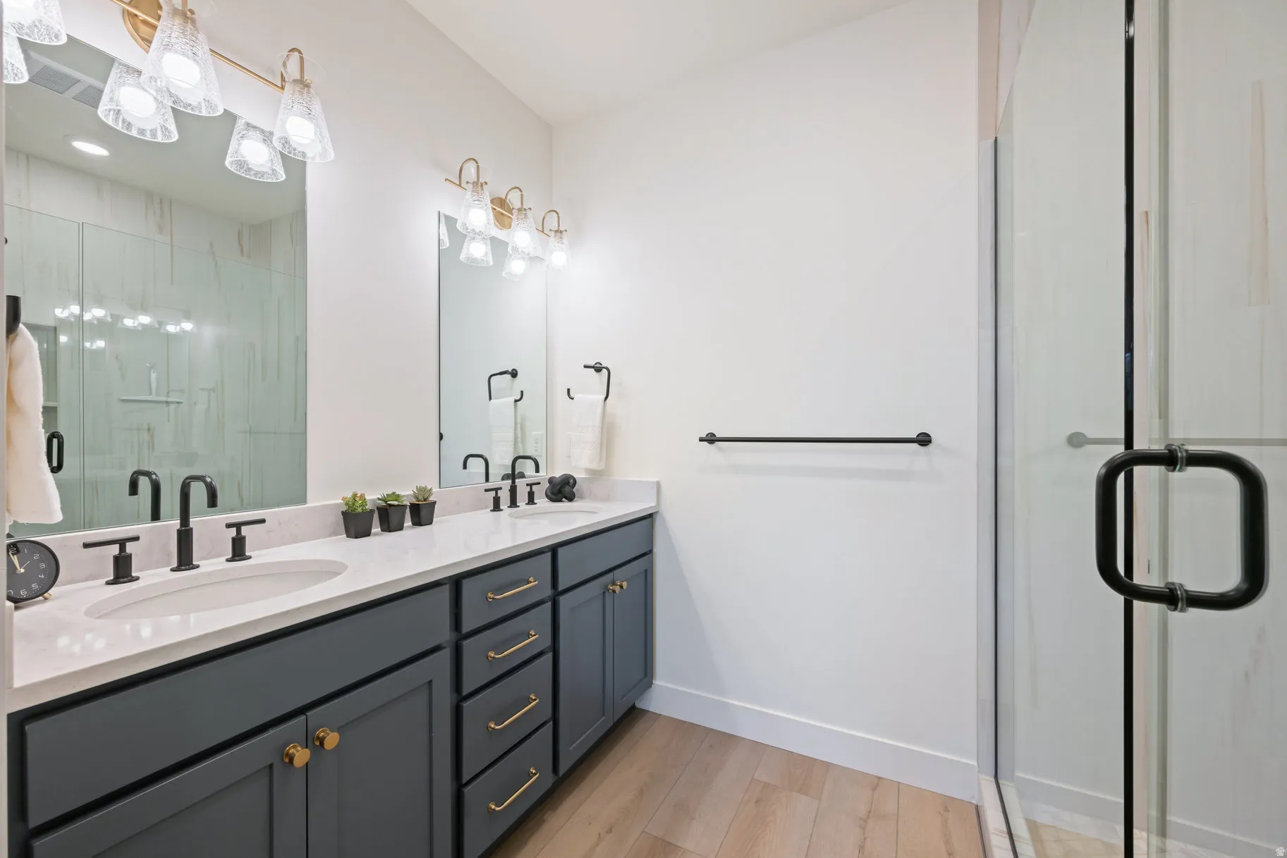 Full bath featuring a shower stall, double vanity, and light wood-style floors